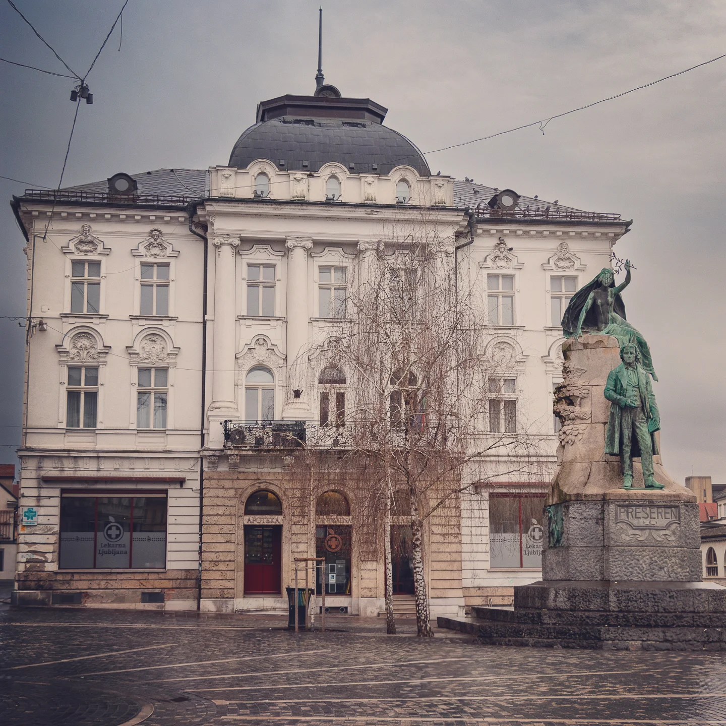 The Prešeren Monument stands beside a stately white building with a domed roof and intricate baroque details.