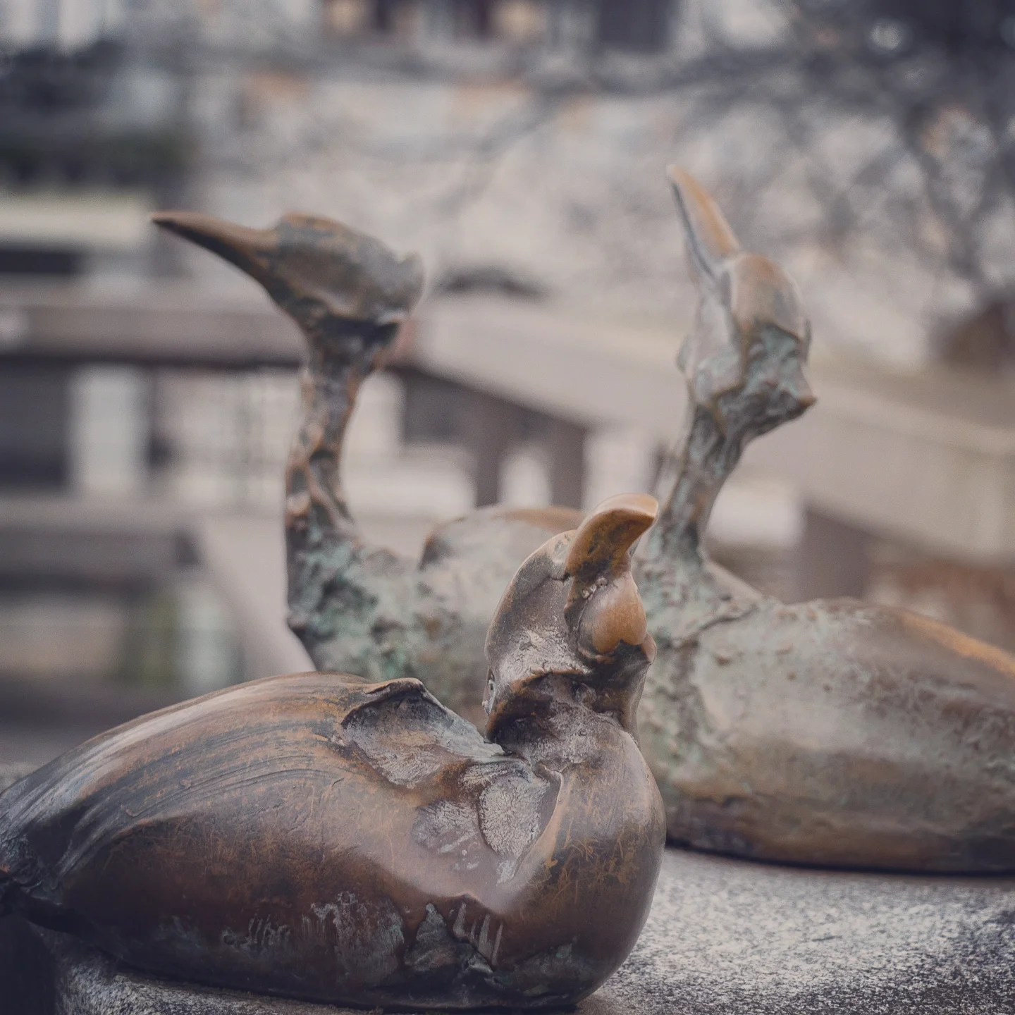 A close-up of two bronze bird sculptures in relaxed, humorous poses on a bridge railing.