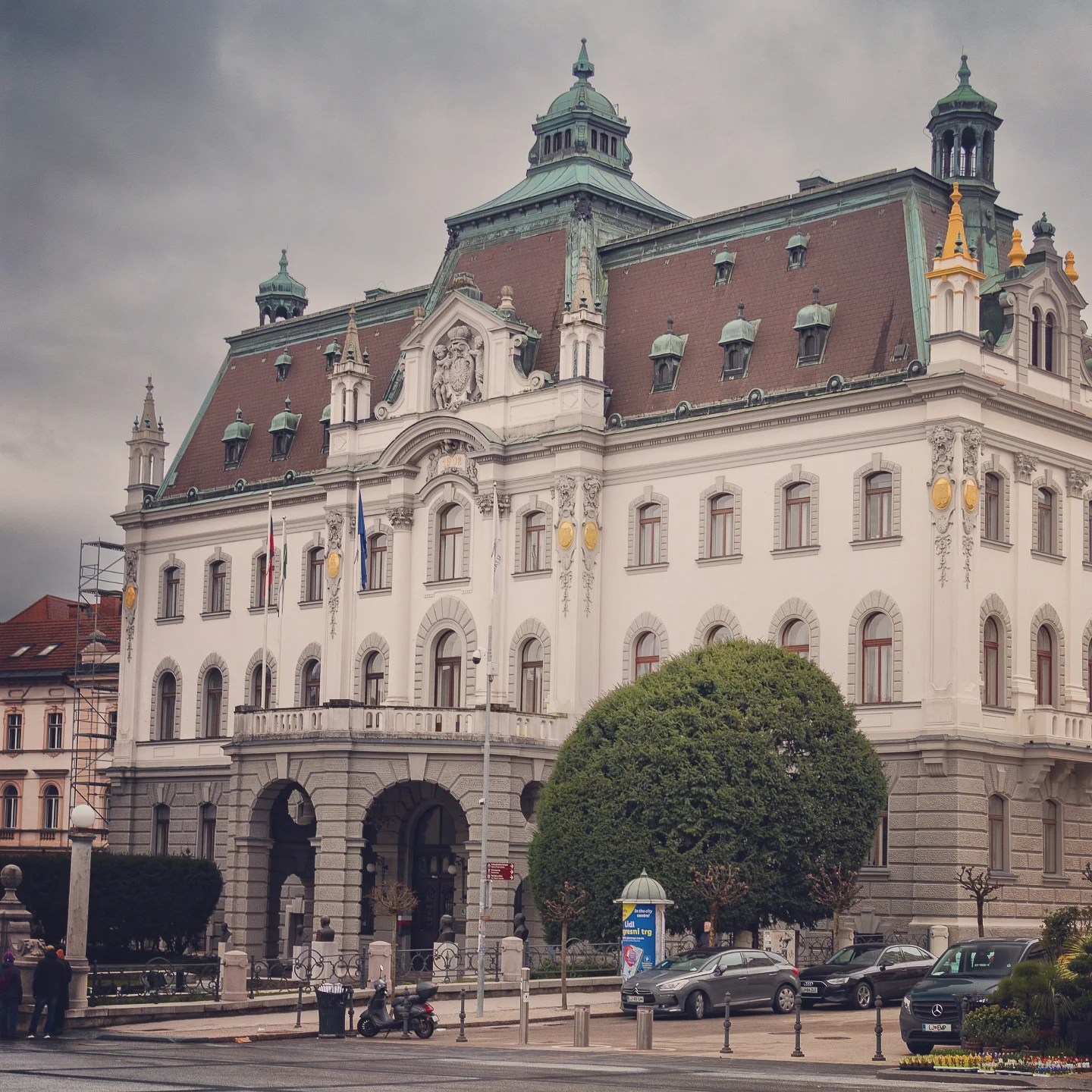 The ornate University of Ljubljana building stands with its green copper spires and white stone detailing under gray skies.