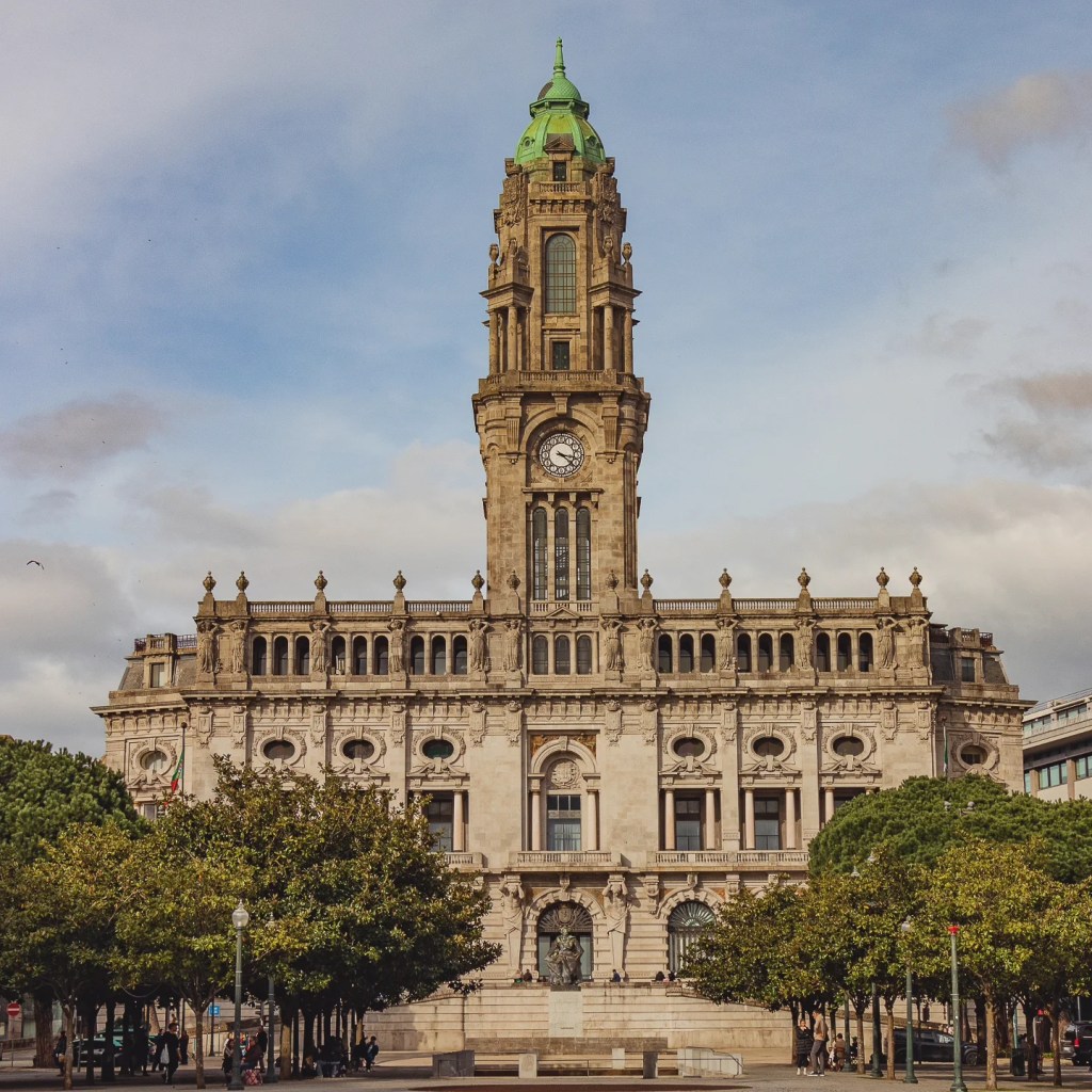 Porto City Hall building with its iconic clock tower and green dome under a partly cloudy sky.