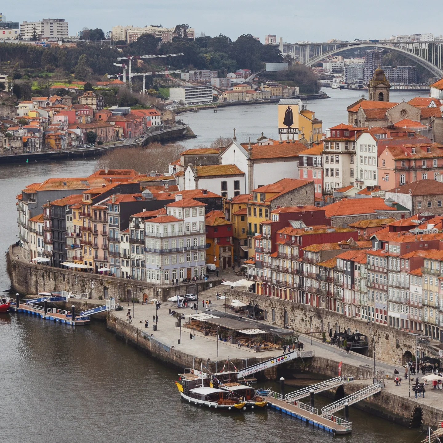Aerial view of Porto’s Ribeira district with colorful buildings along the Douro River and Sandeman Port Wine sign in the distance.
