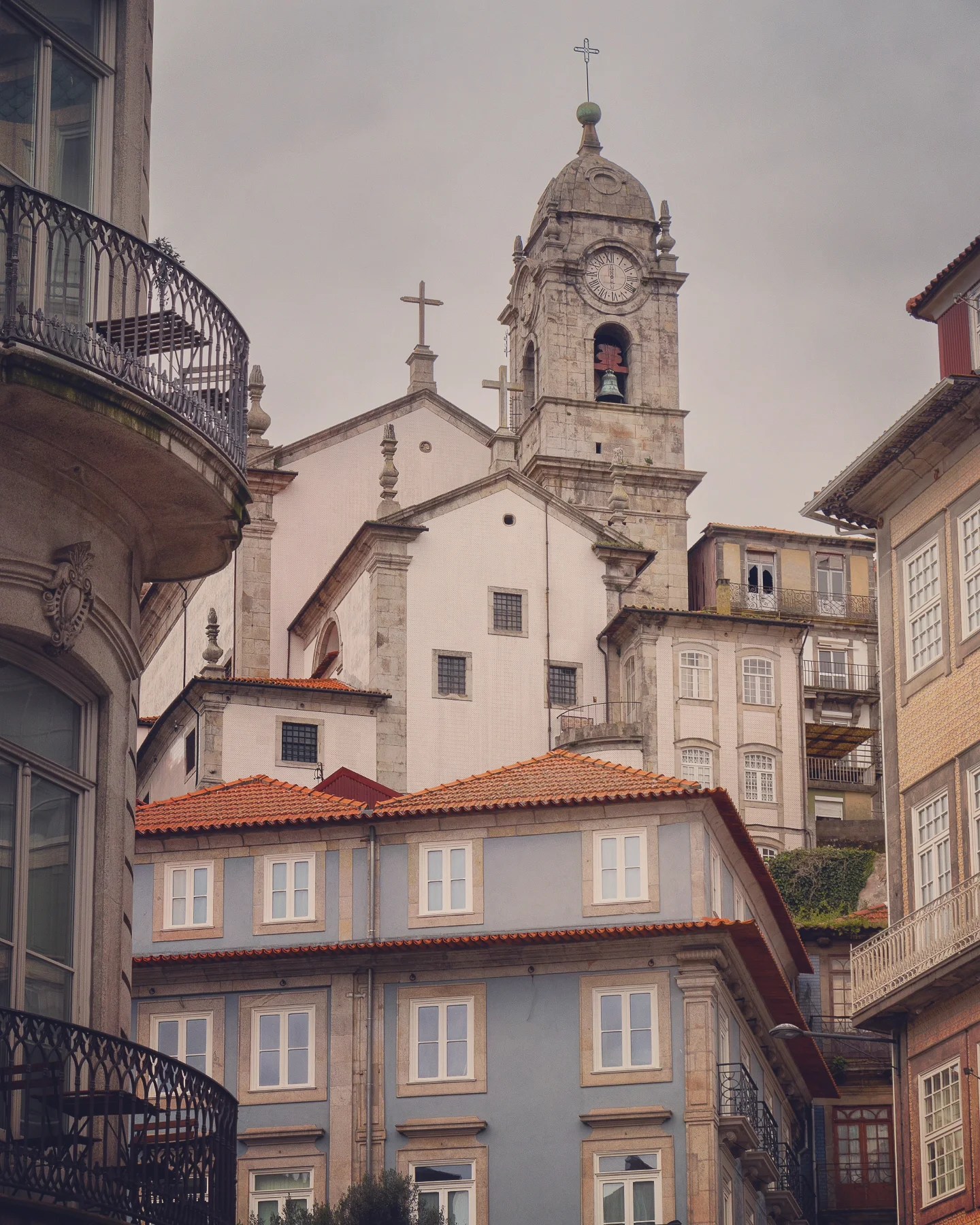 Church bell tower with clock face rising above pastel-colored buildings in Porto, Portugal.