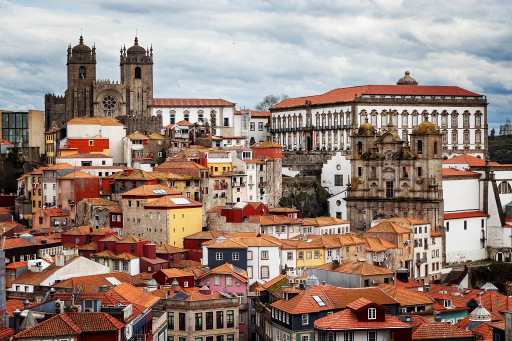 Panoramic view over Porto’s red rooftops with the Porto Cathedral and Episcopal Palace in the distance under a cloudy sky.