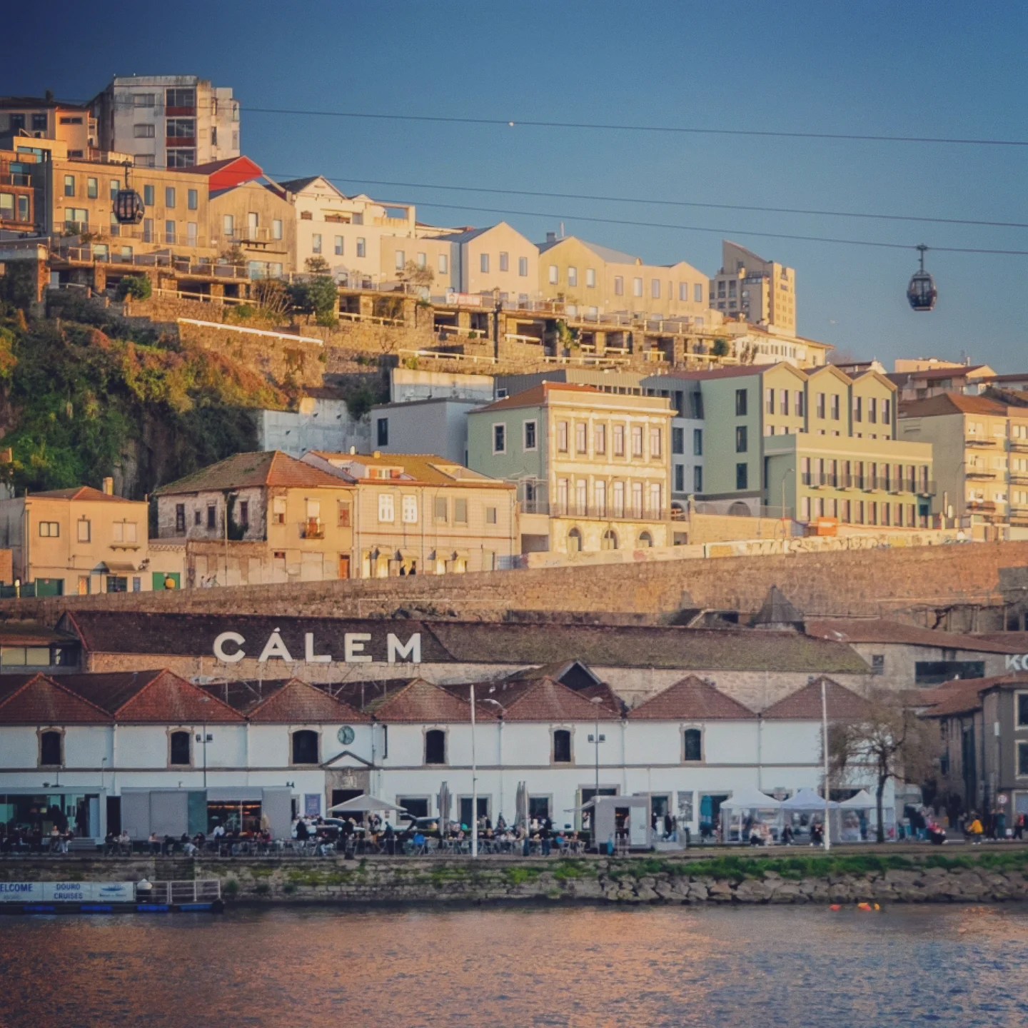 View of the white Caves Cálem building along the Douro River with colorful houses in the background.