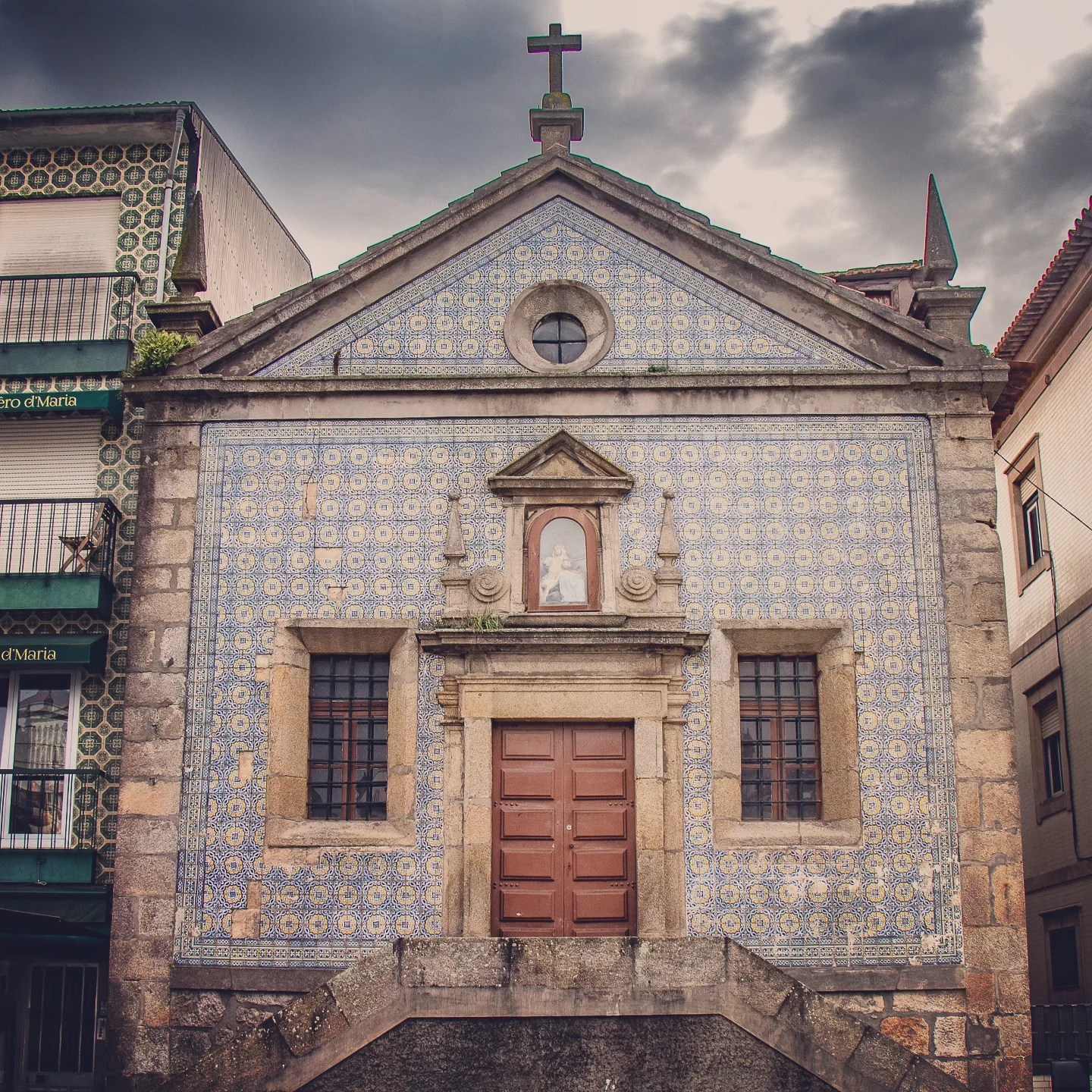 Front view of a small chapel covered in blue and white azulejo tiles with a wooden door in Porto.