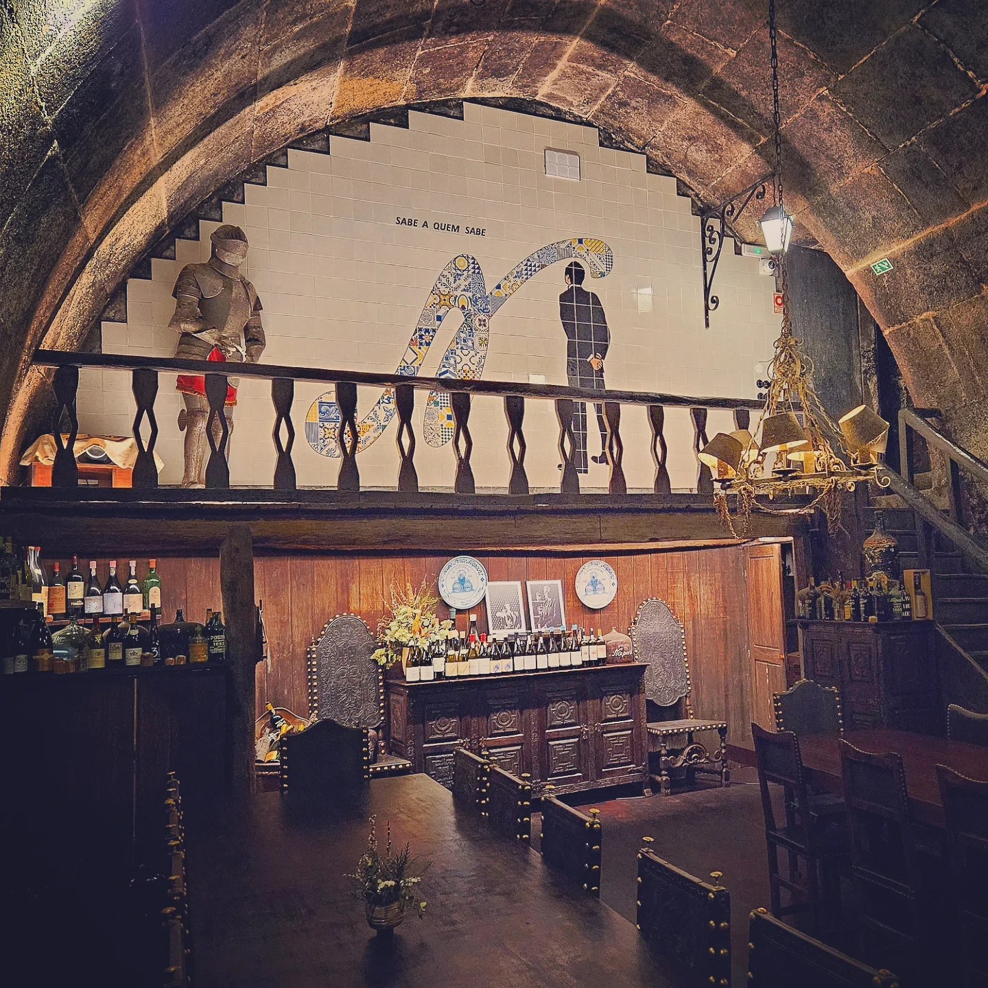 Rustic tasting room inside a Porto wine cellar featuring a large tile mural and a knight statue.