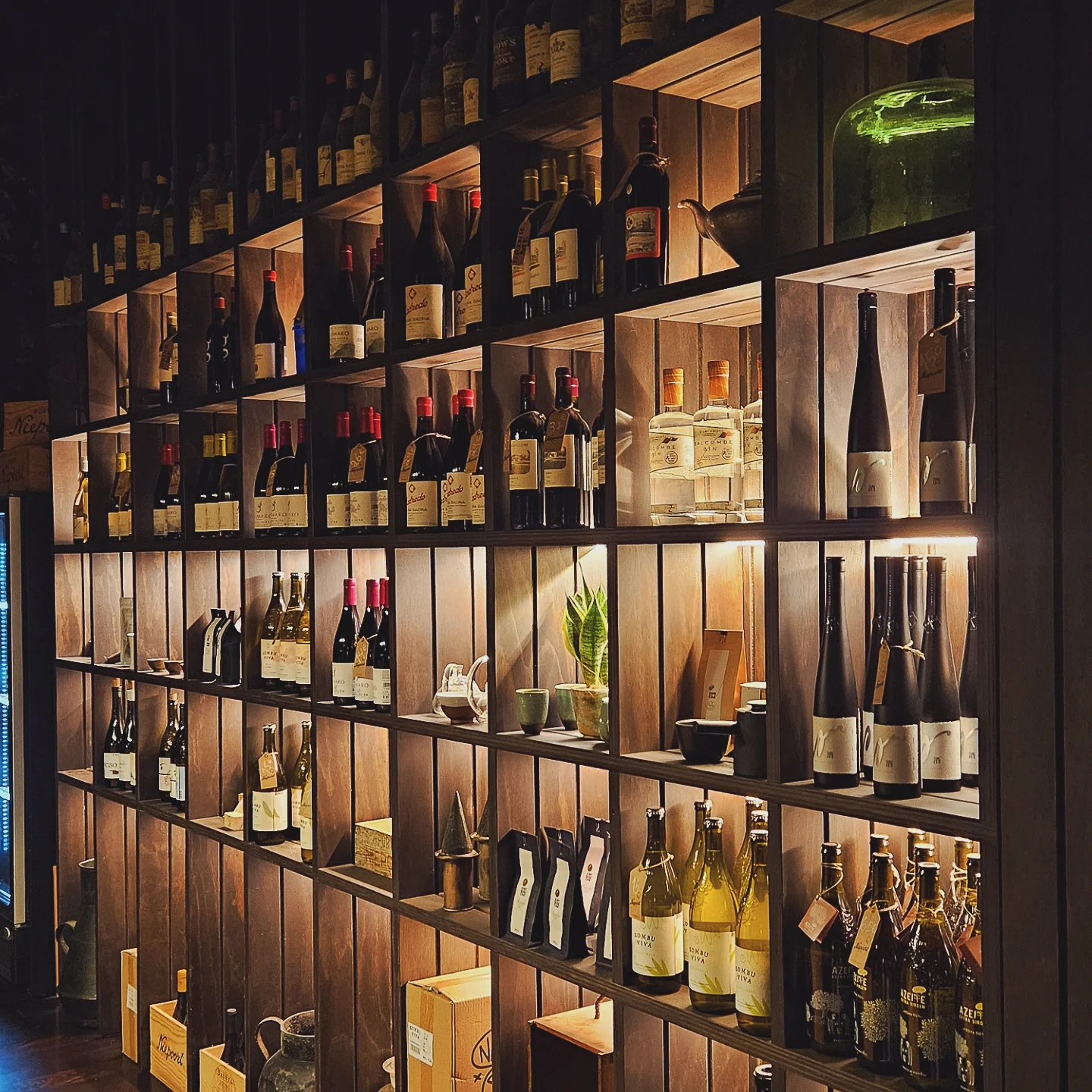 Modern backlit wooden shelves filled with various wine bottles and gourmet products for sale at Niepoort.