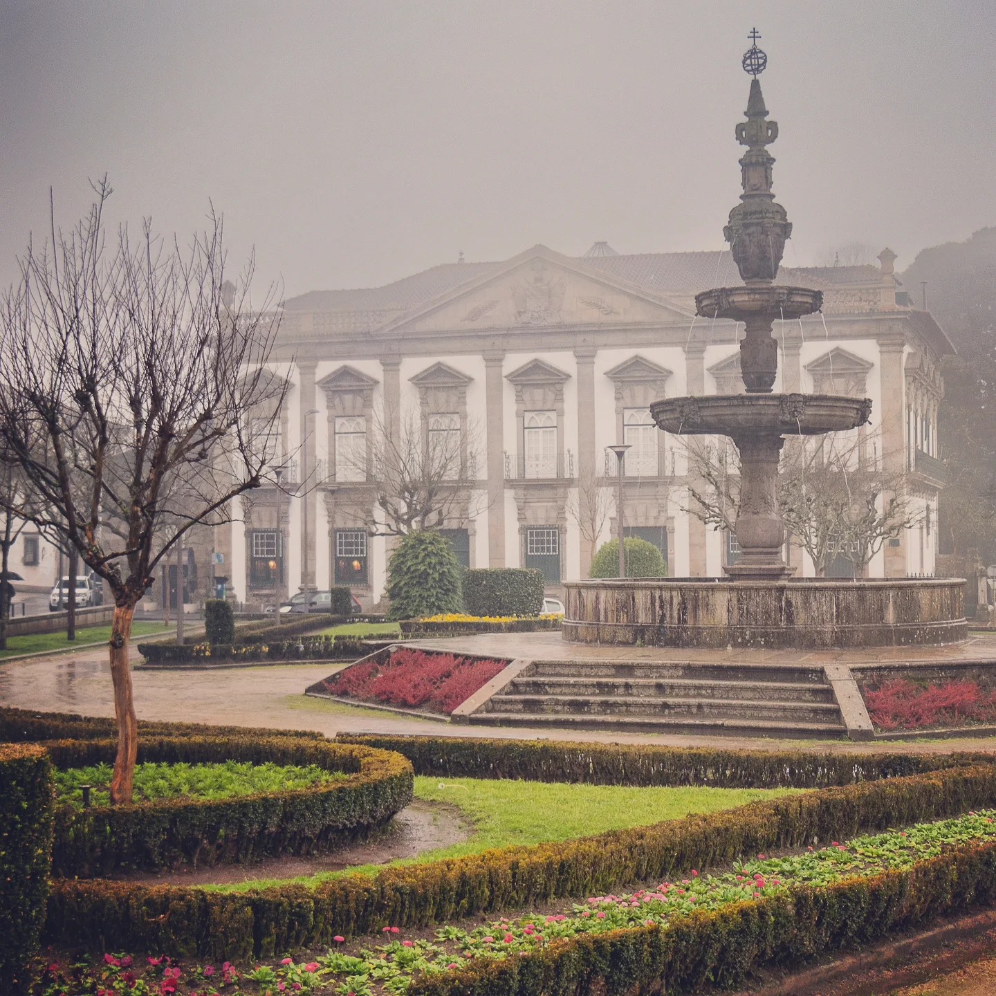 Foggy garden with a stone fountain and a historic building in Braga, Portugal.