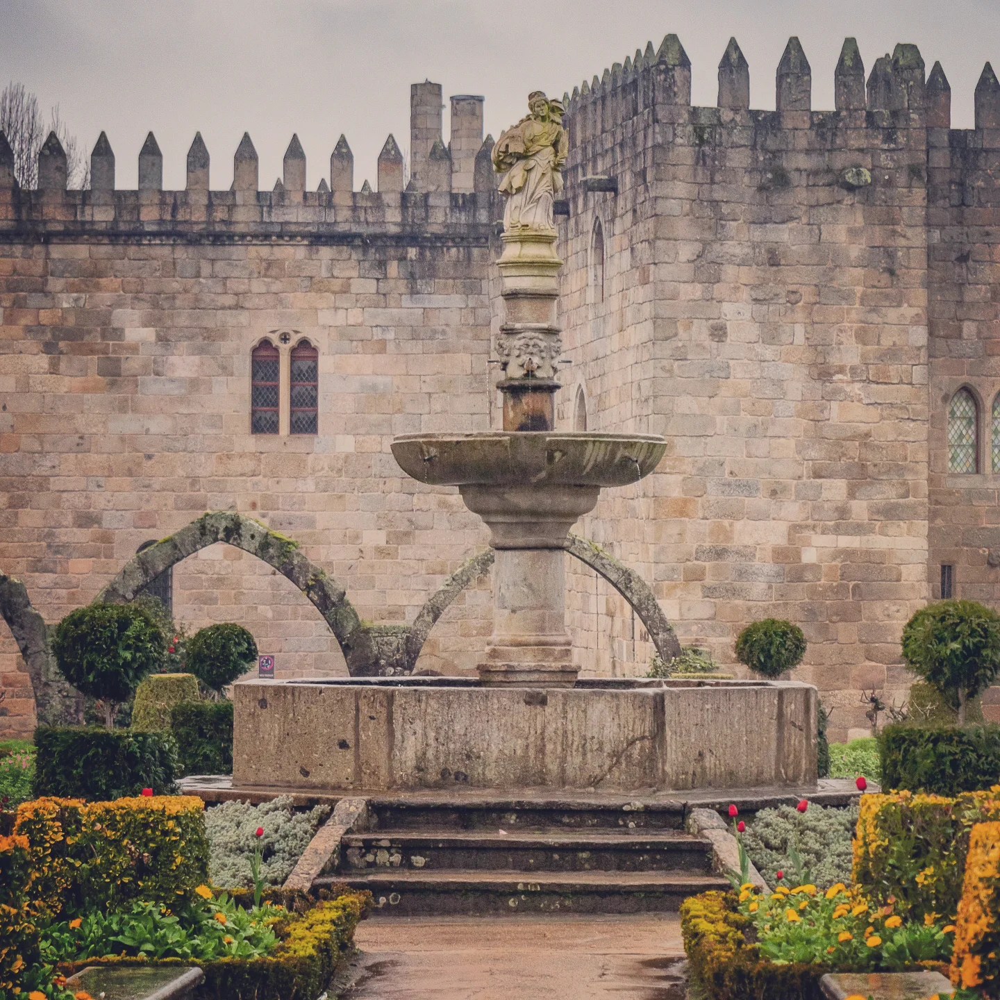 Fountain with stone statue and fortress-like medieval walls in Braga, Portugal.