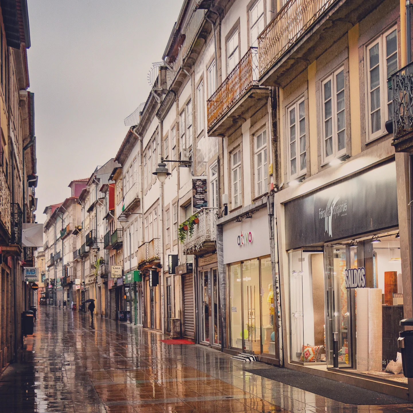 Narrow cobblestone shopping street with historic buildings and wet pavement in Braga, Portugal.