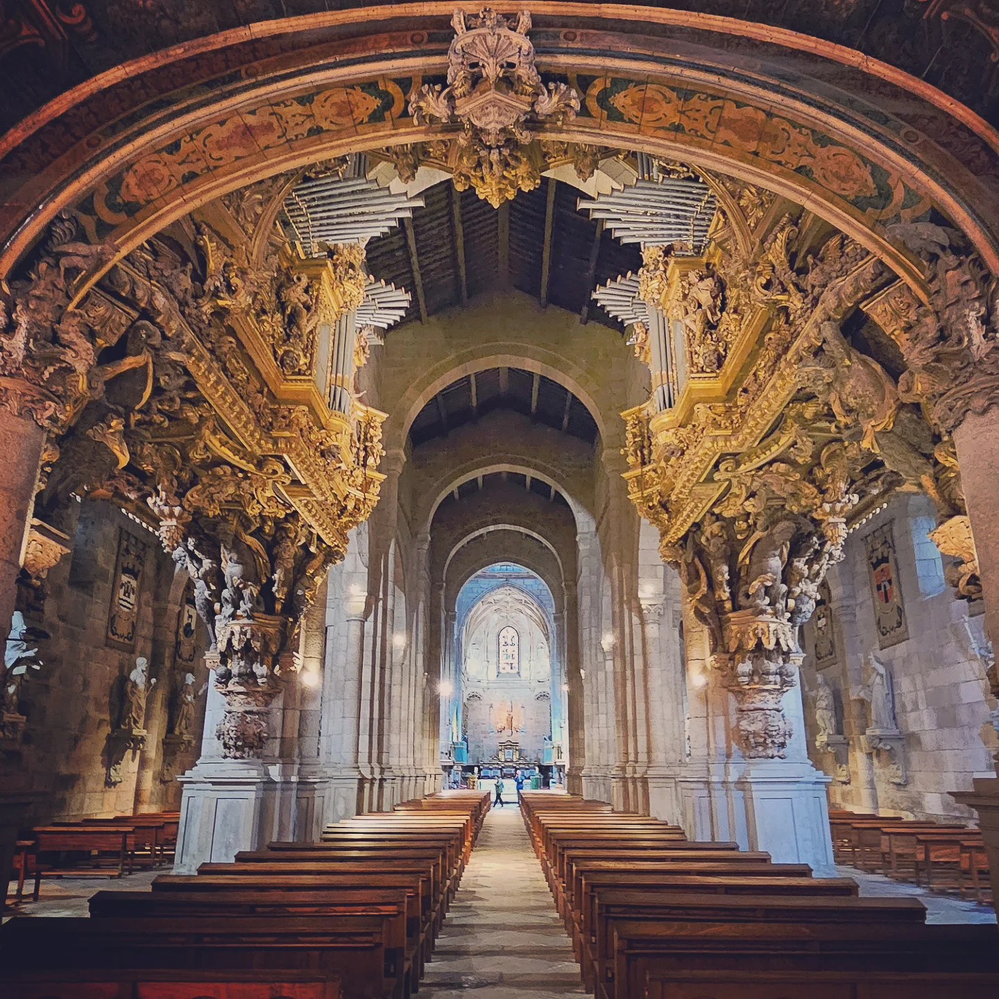 Ornate interior nave of Braga Cathedral with carved stone arches, gold leaf details, and wooden pews.