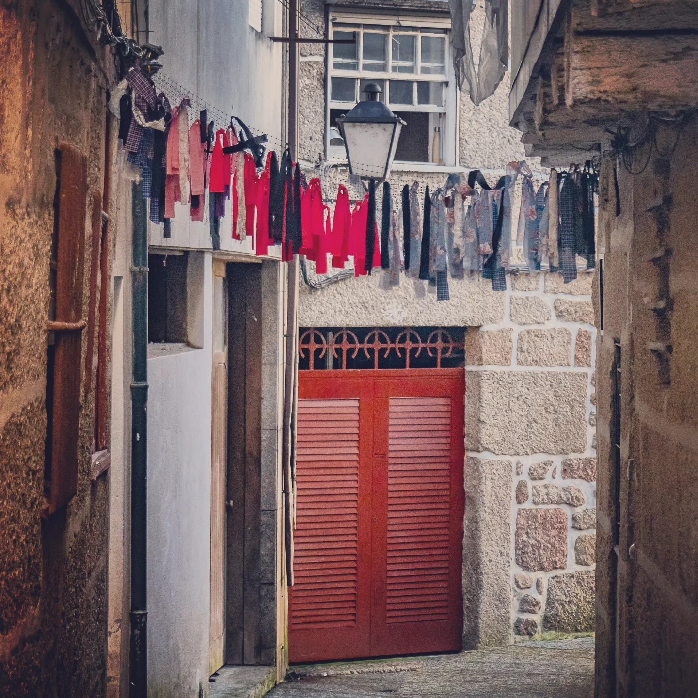 Colorful ribbons hanging on lines above a narrow cobblestone alley in Guimarães old town, Portugal.
