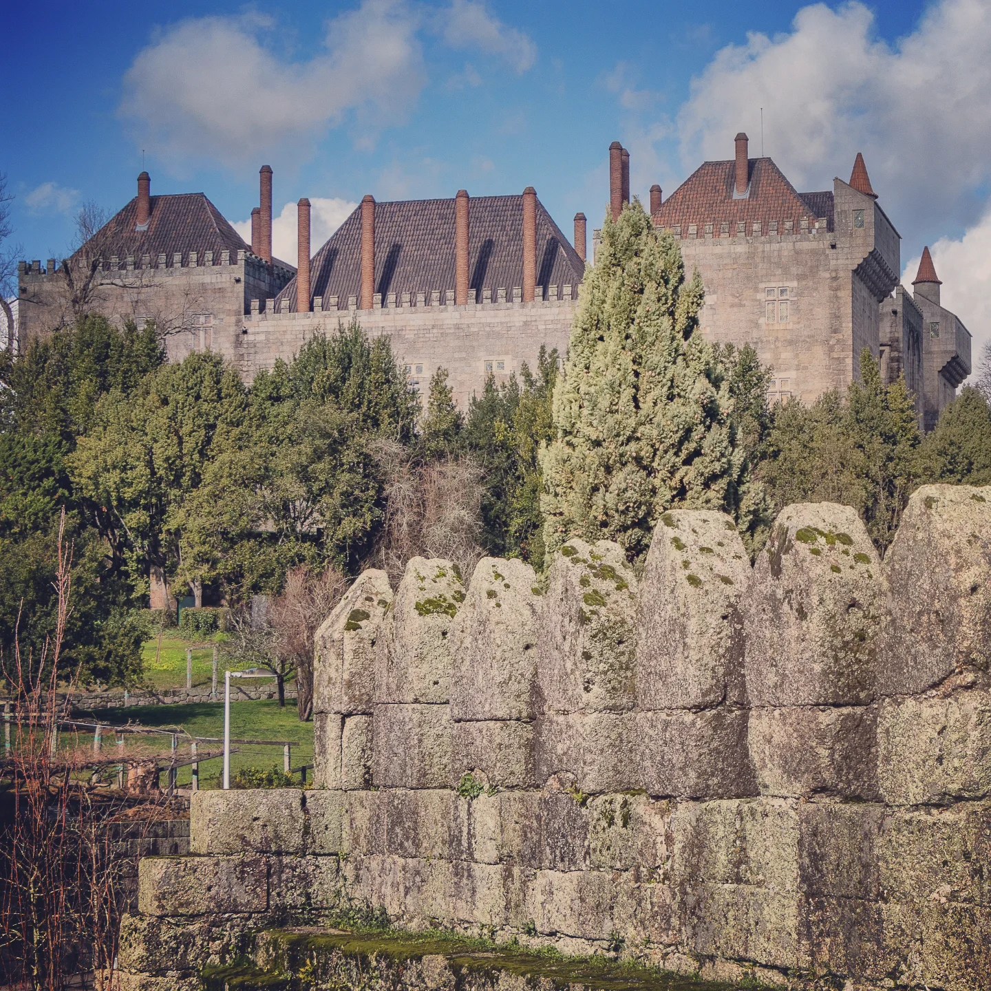 Palace of the Dukes of Braganza in Guimarães, seen above mossy stone walls and dense green trees.