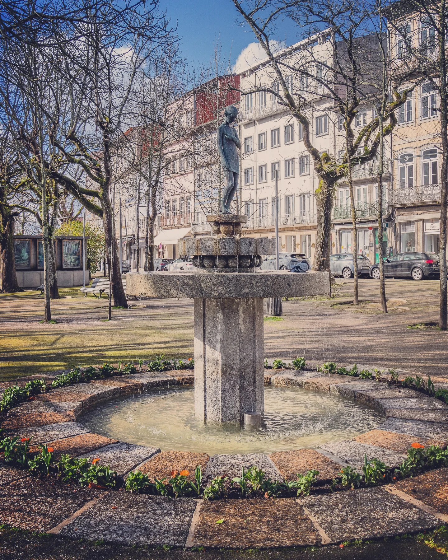 Stone fountain with a bronze child statue in a leafy square in Guimarães.