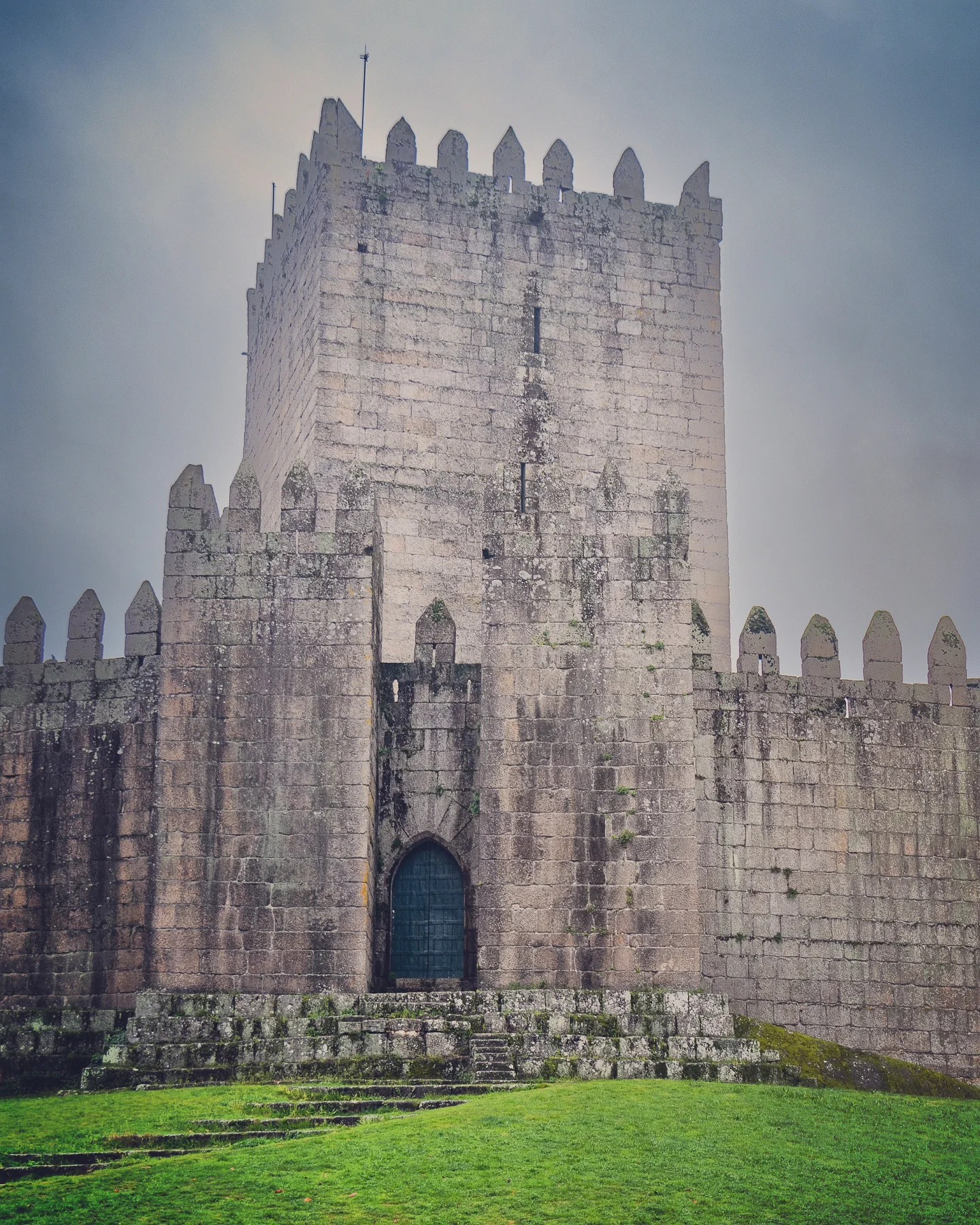 Front view of Guimarães Castle’s main tower and fortified stone walls on a misty day, with the arched main gate visible at the center.
