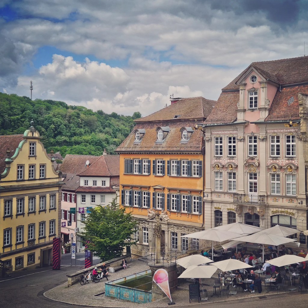 A picturesque view of Schwäbisch Hall featuring charming half-timbered buildings and a plaza with outdoor seating under umbrellas.