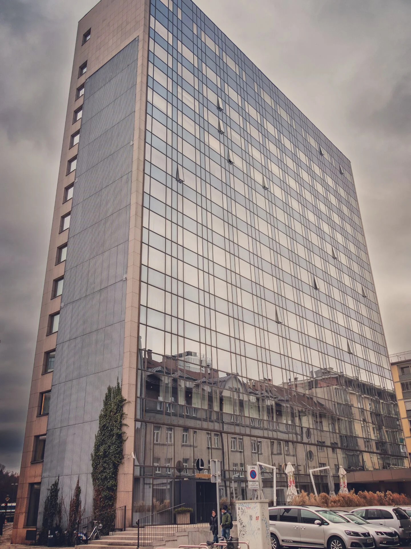 Tall glass building reflecting nearby historic structures, with a moody sky overhead.