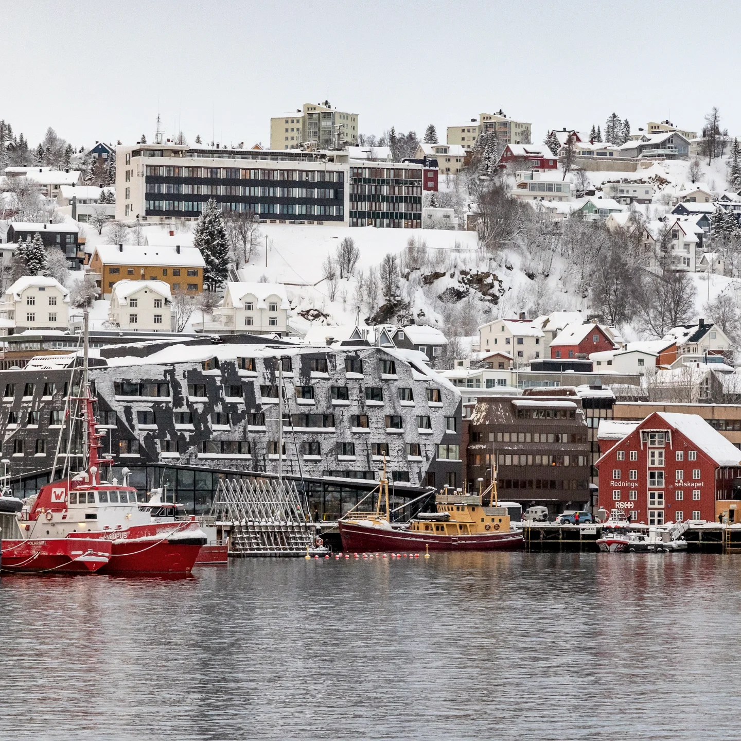 Snow-covered buildings and colorful boats along the harbor in Tromsø, Norway.
