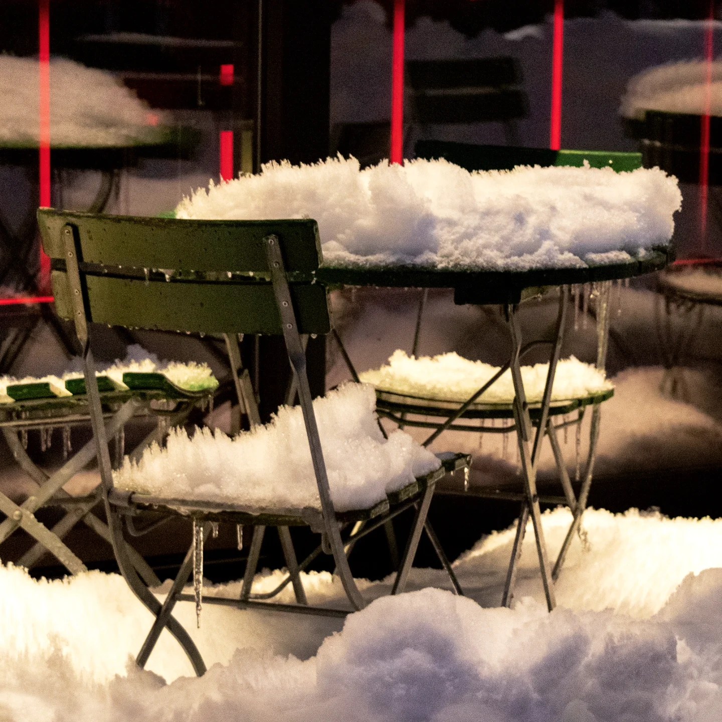 Outdoor café chairs and tables blanketed in thick snow, glowing softly in the evening light—an atmospheric glimpse of winter in Tromsø.