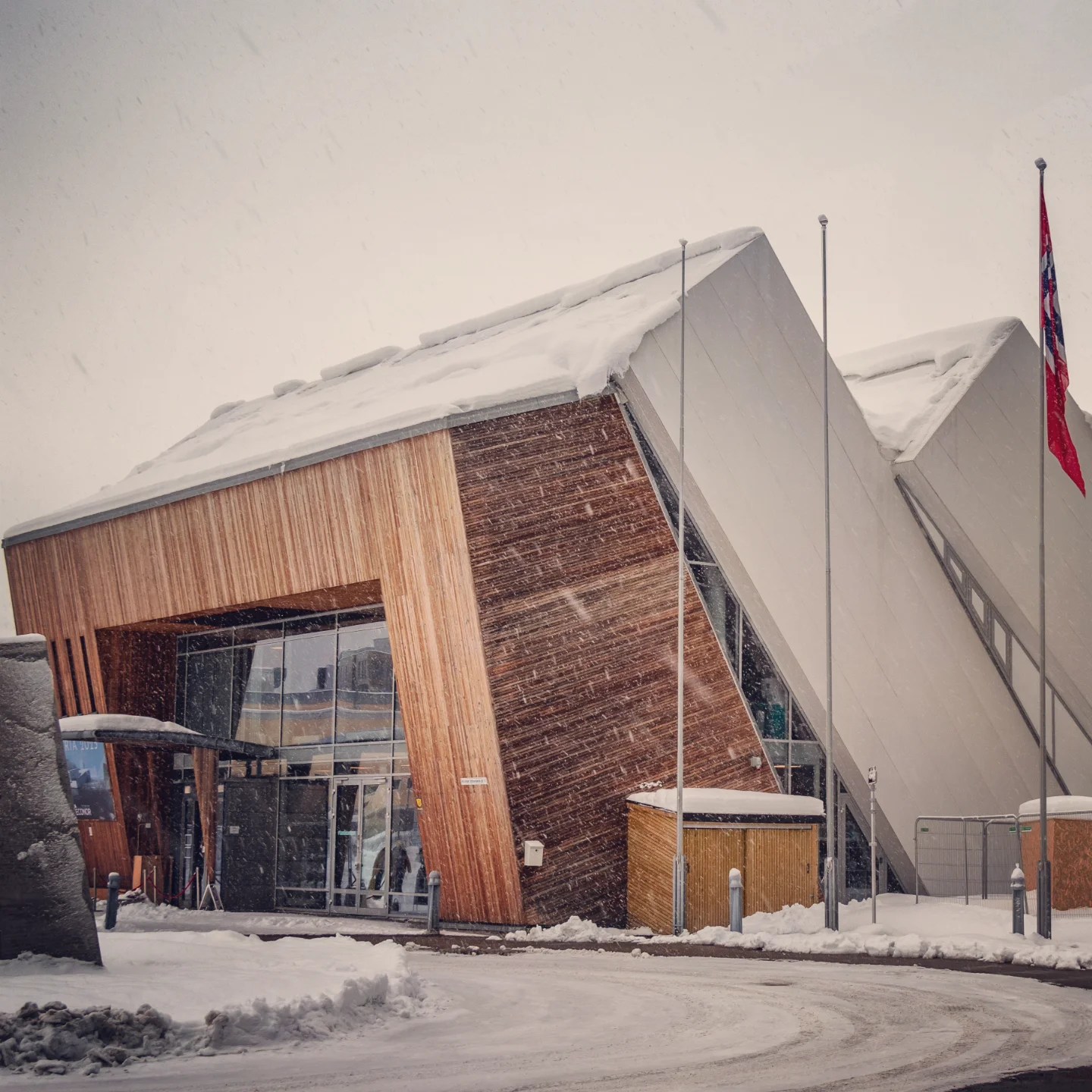 Modern, angular wooden and metal building with snow piled on the roof during snowfall—Polaria Arctic experience center in Tromsø.