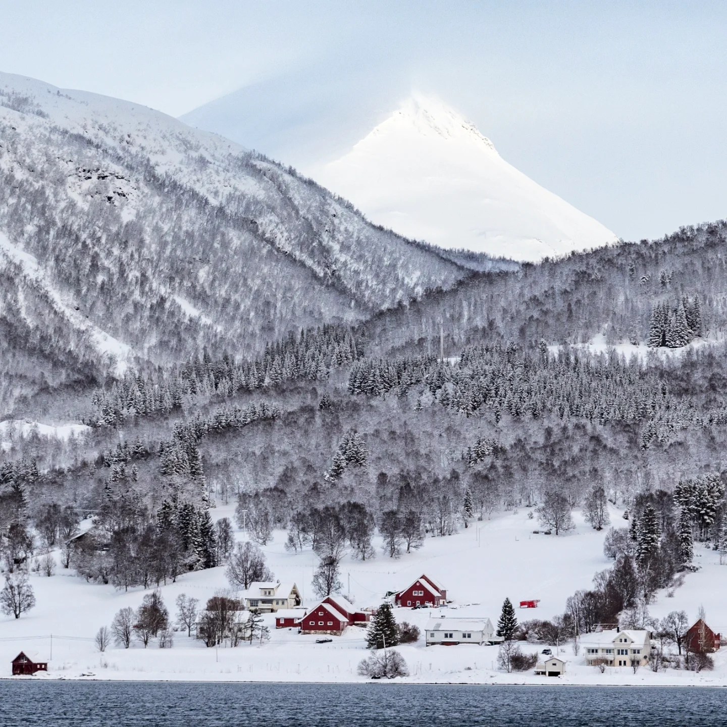 Cluster of red and white homes with snow-dusted trees and a towering peak behind.