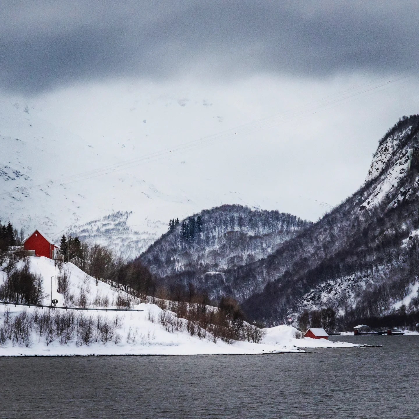 Dramatic valley view with red cabins nestled below steep, snowy slopes.