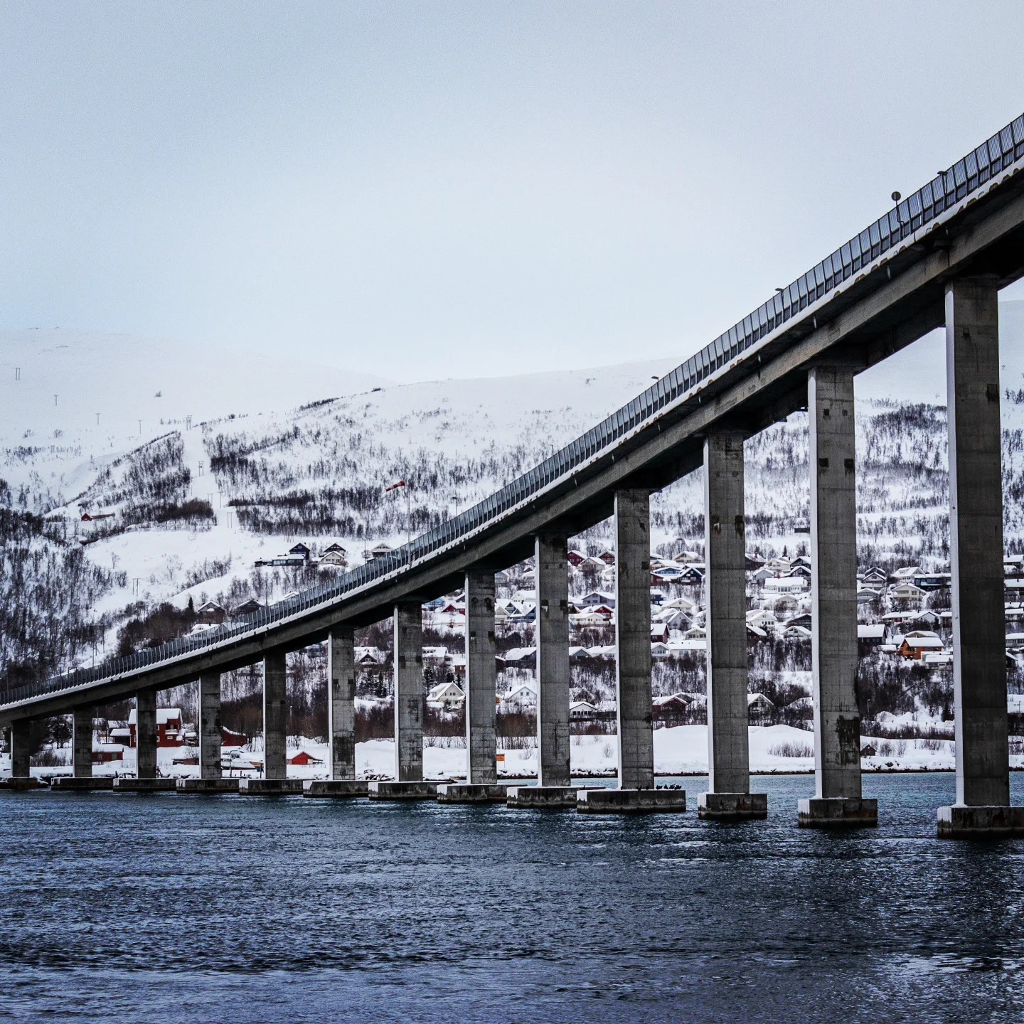 An elegant arc of Tromsø Bridge stretches high above the water, connecting the snowy hillsides on either side.