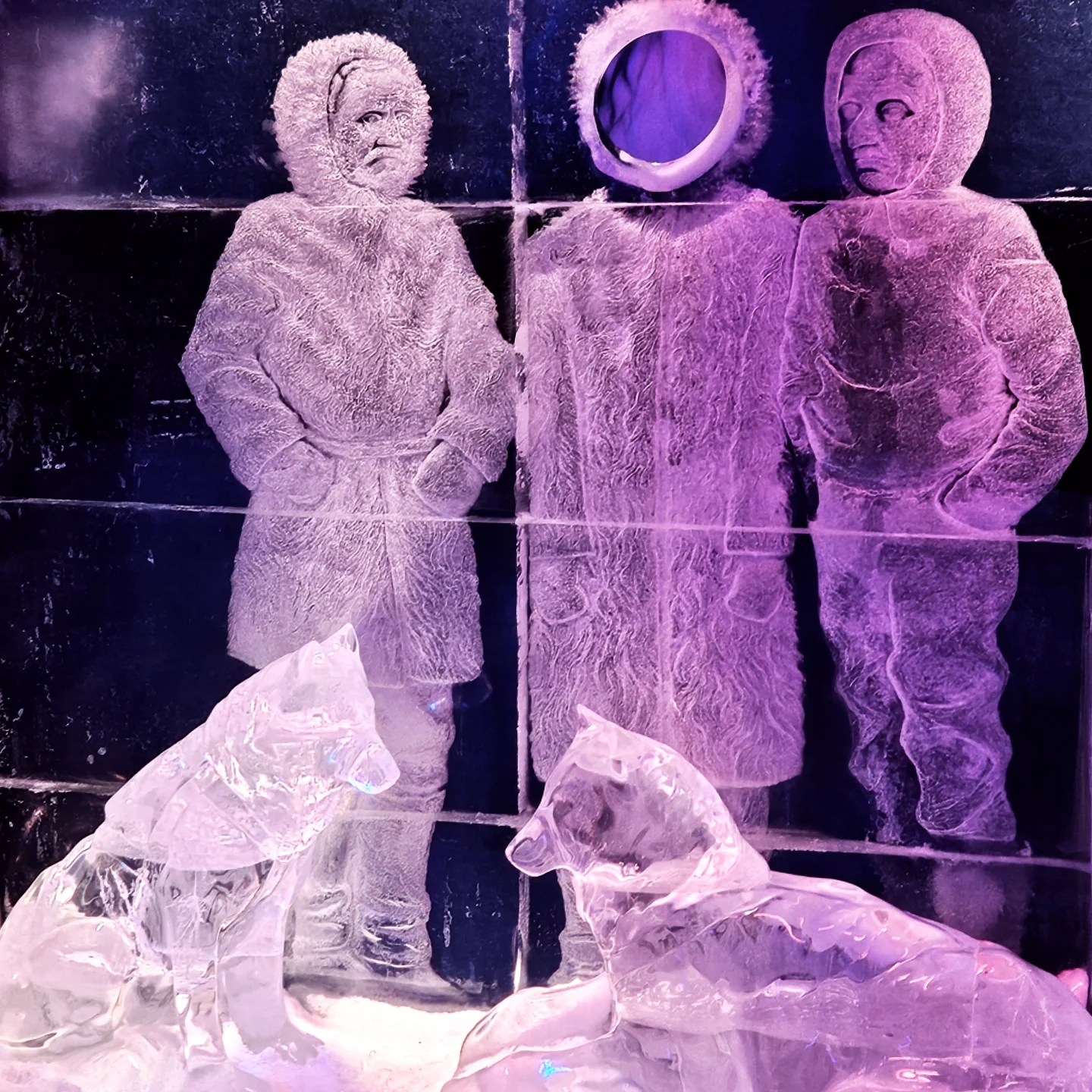 Intricate ice sculptures and carvings of explorers and sled dogs glow under purple light, creating a frozen Arctic tableau.
