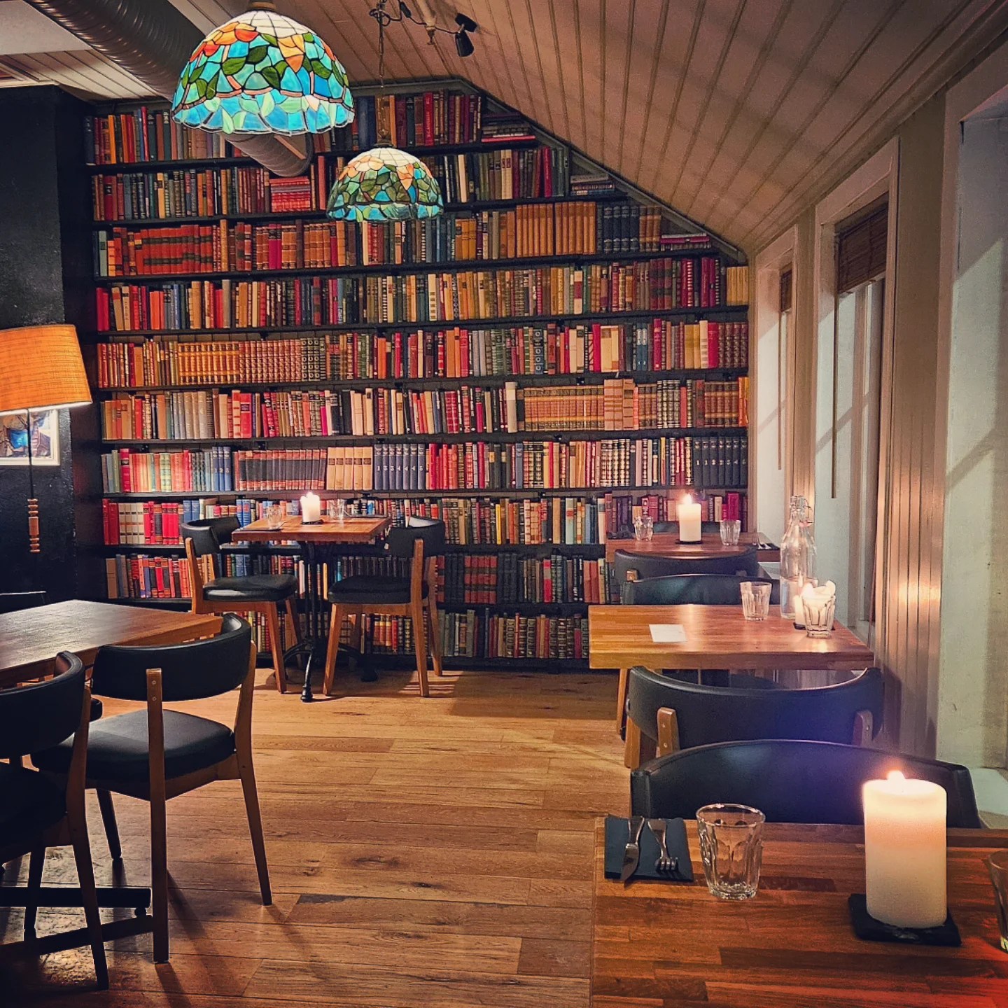 A cozy restaurant interior lined with bookshelves and glowing candles, offering a quiet literary dining atmosphere.