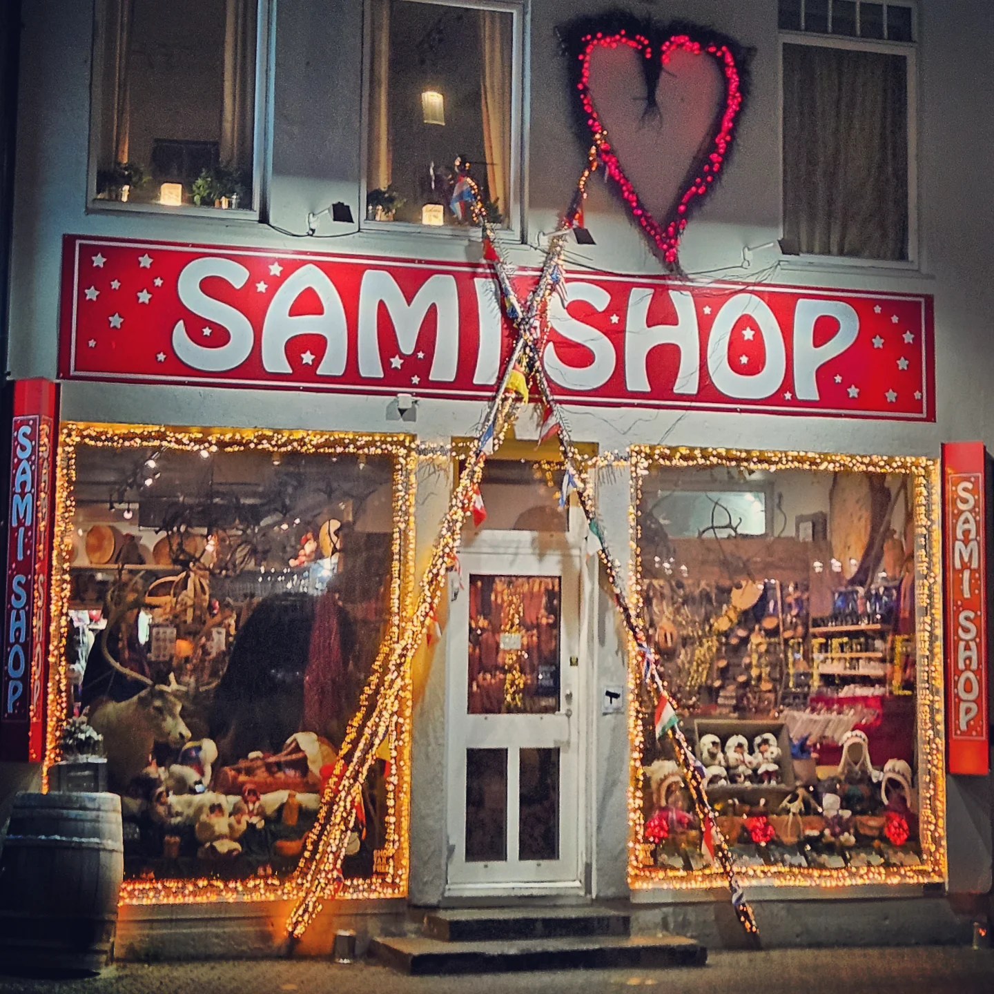 A festive Sami souvenir shop decorated with lights and hearts, reindeer figurines and fur hats glowing in the window.