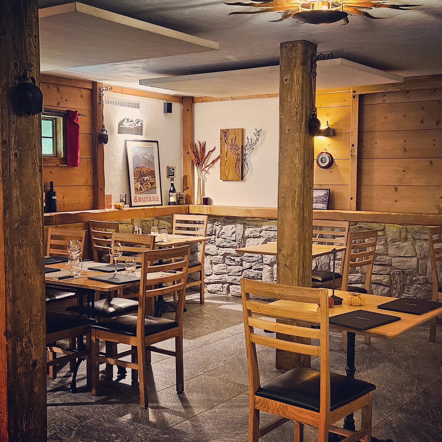 Warm wood-panelled and stone-walled dining room with simple wooden tables and chairs, alpine décor and a vintage Gruyère ski poster.