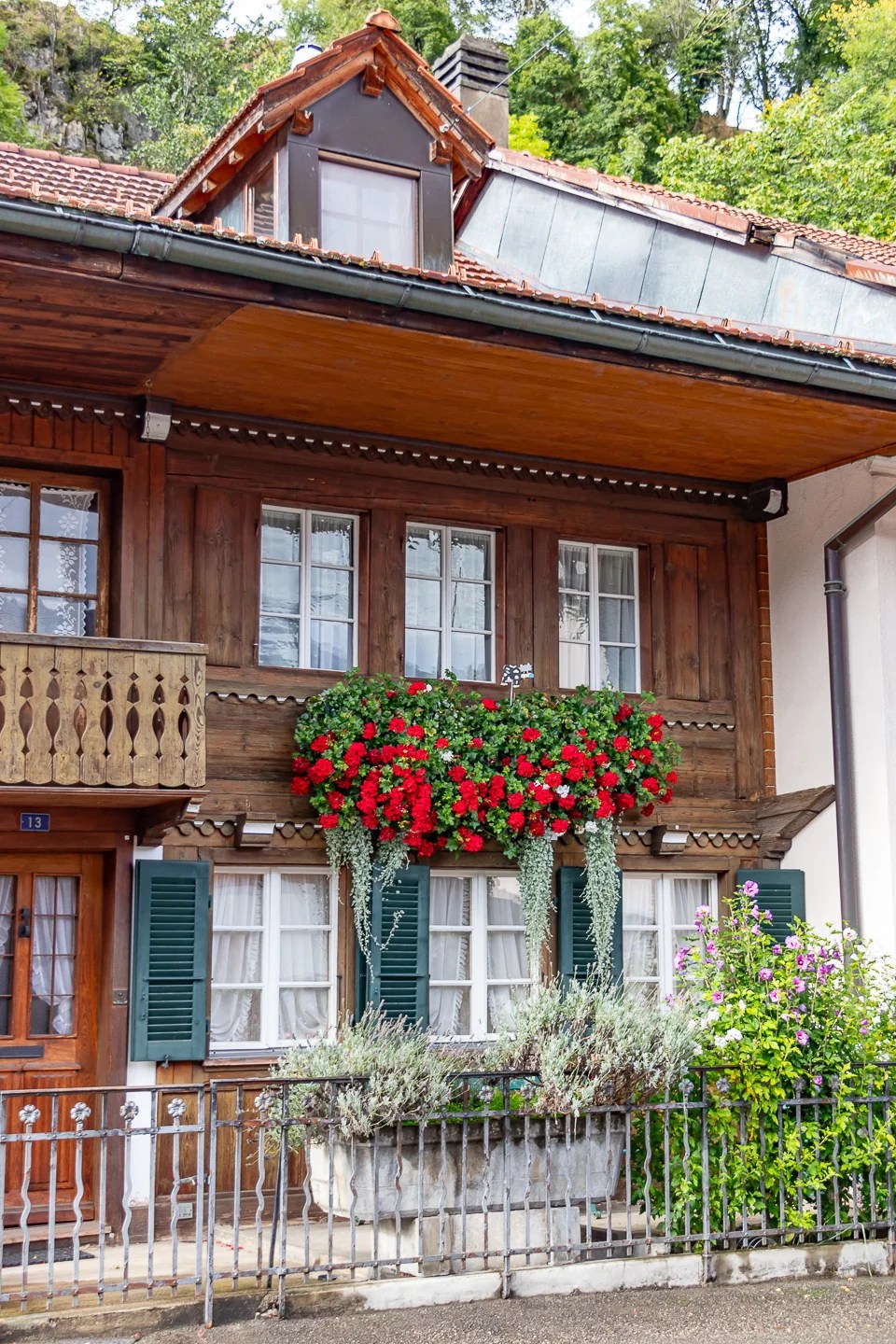 Close-up of a timber façade with green shutters and a cascade of red geraniums on the balcony in Charmey.