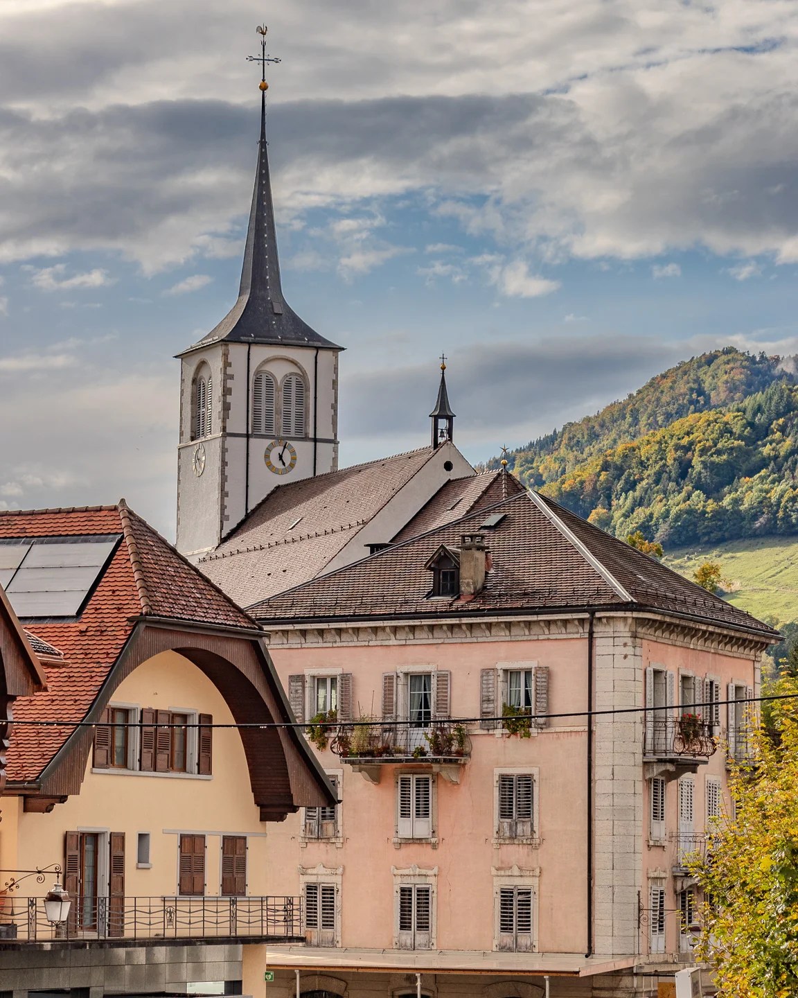 Saint-Pierre-aux-Liens church tower rising above pastel village roofs with forested hillside beyond.