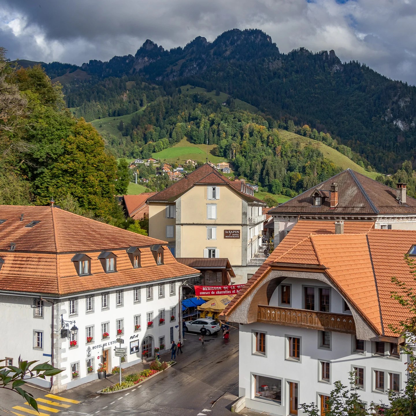 levated view over Charmey’s terracotta rooftops toward a jagged Pre-Alps ridge under shifting clouds.