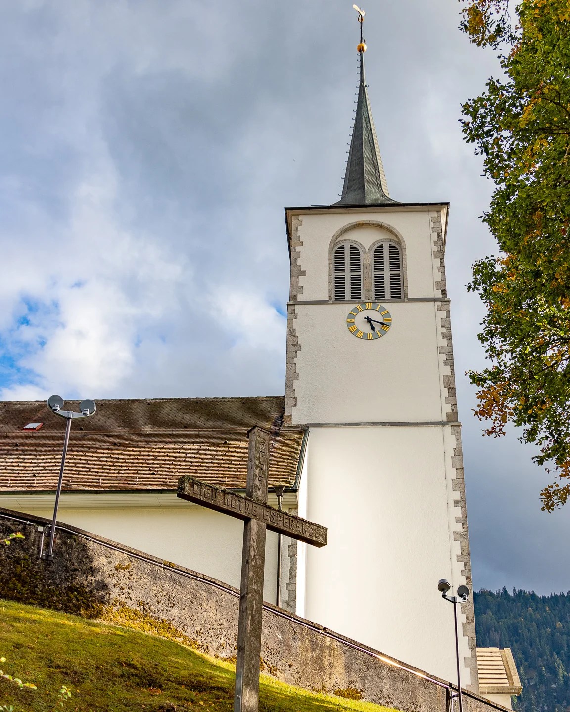 Detail of Saint-Pierre-aux-Liens steeple and weather-worn wooden cross under a dramatic sky.