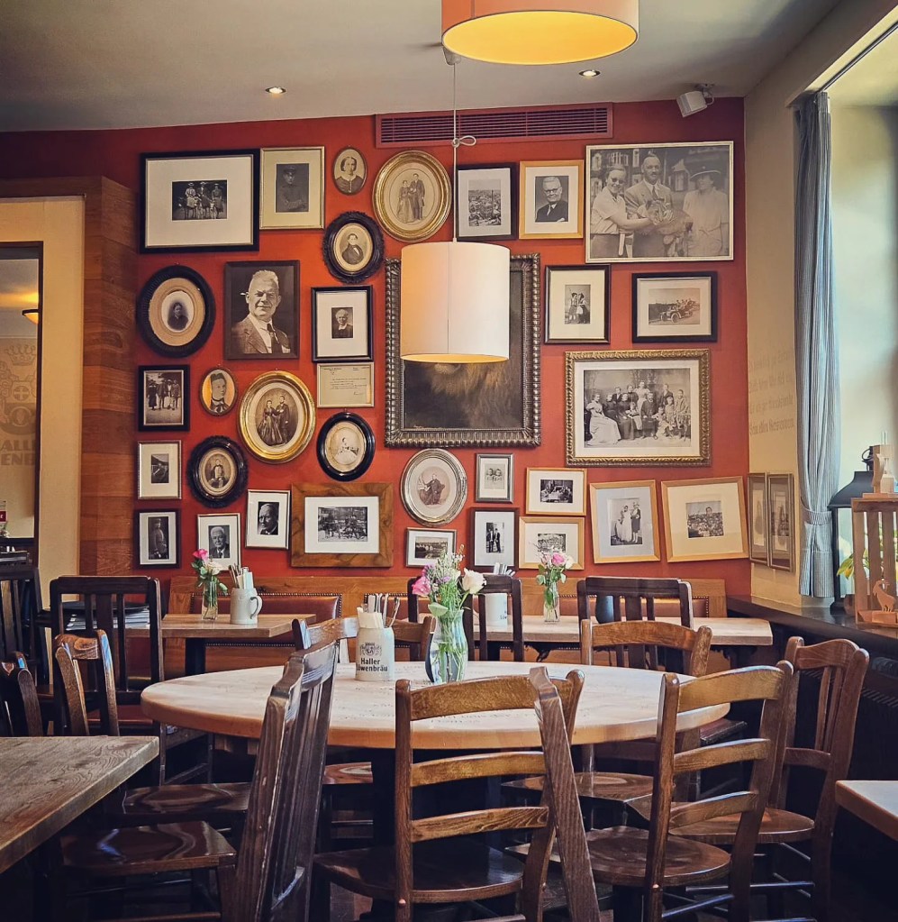 The cozy interior of Brauereiausschank zum Löwen in Schwäbisch Hall, featuring wooden tables, floral centerpieces, and a wall covered in framed historic family photos and portraits.