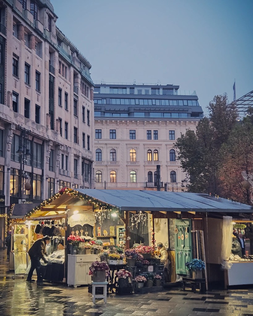 Flower-filled wooden stall at a Budapest Christmas market on a rainy evening.