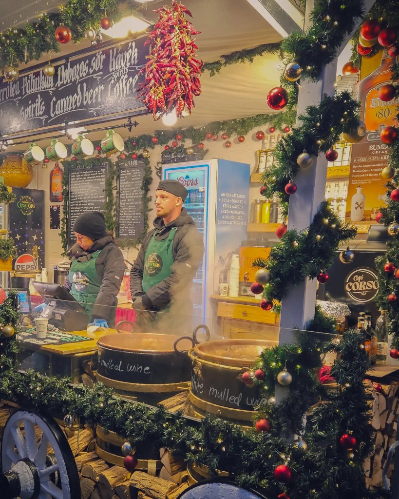 Cauldrons of mulled wine surrounded by festive garlands at a Budapest Christmas market stall.