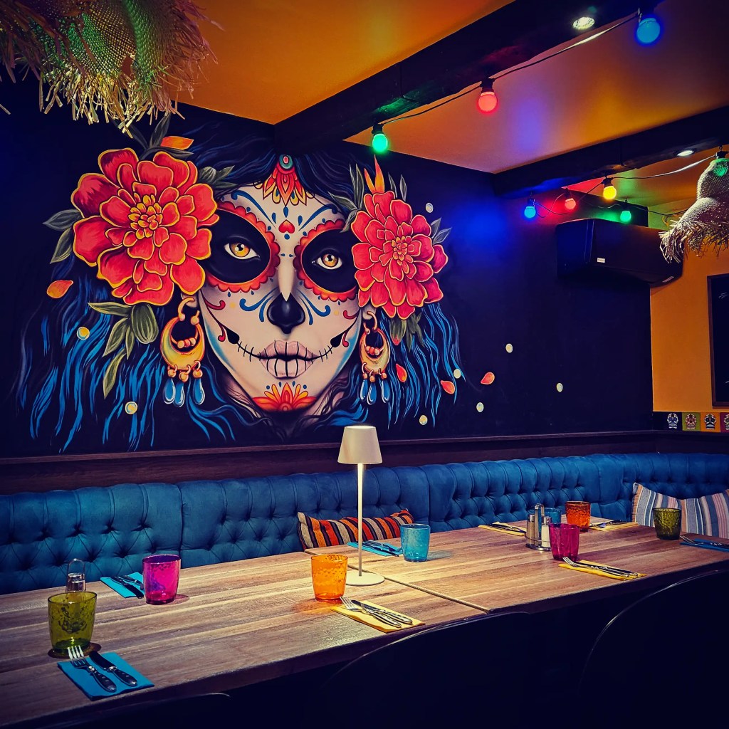 Colorful Day of the Dead mural and festive table setup inside Hugo’s restaurant.