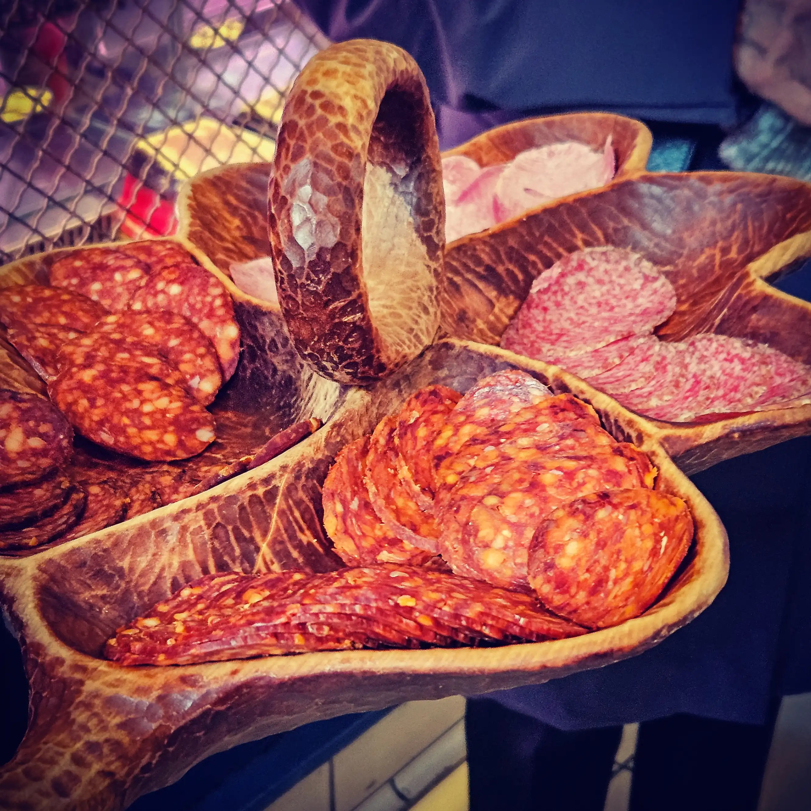 Carved wooden platter filled with slices of Hungarian salami and cured meats.