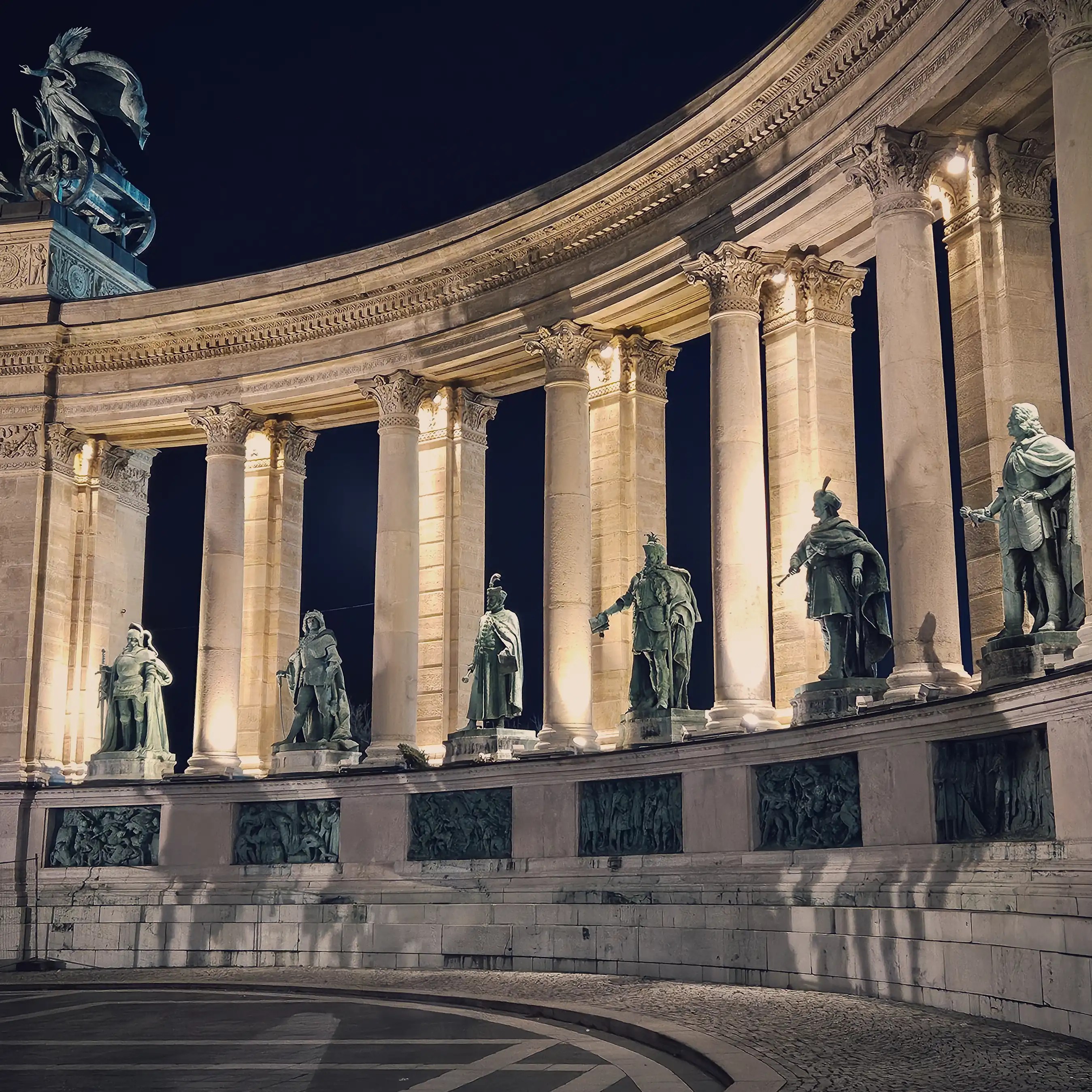 Illuminated statues and colonnade at Budapest’s Hero’s Square at night.