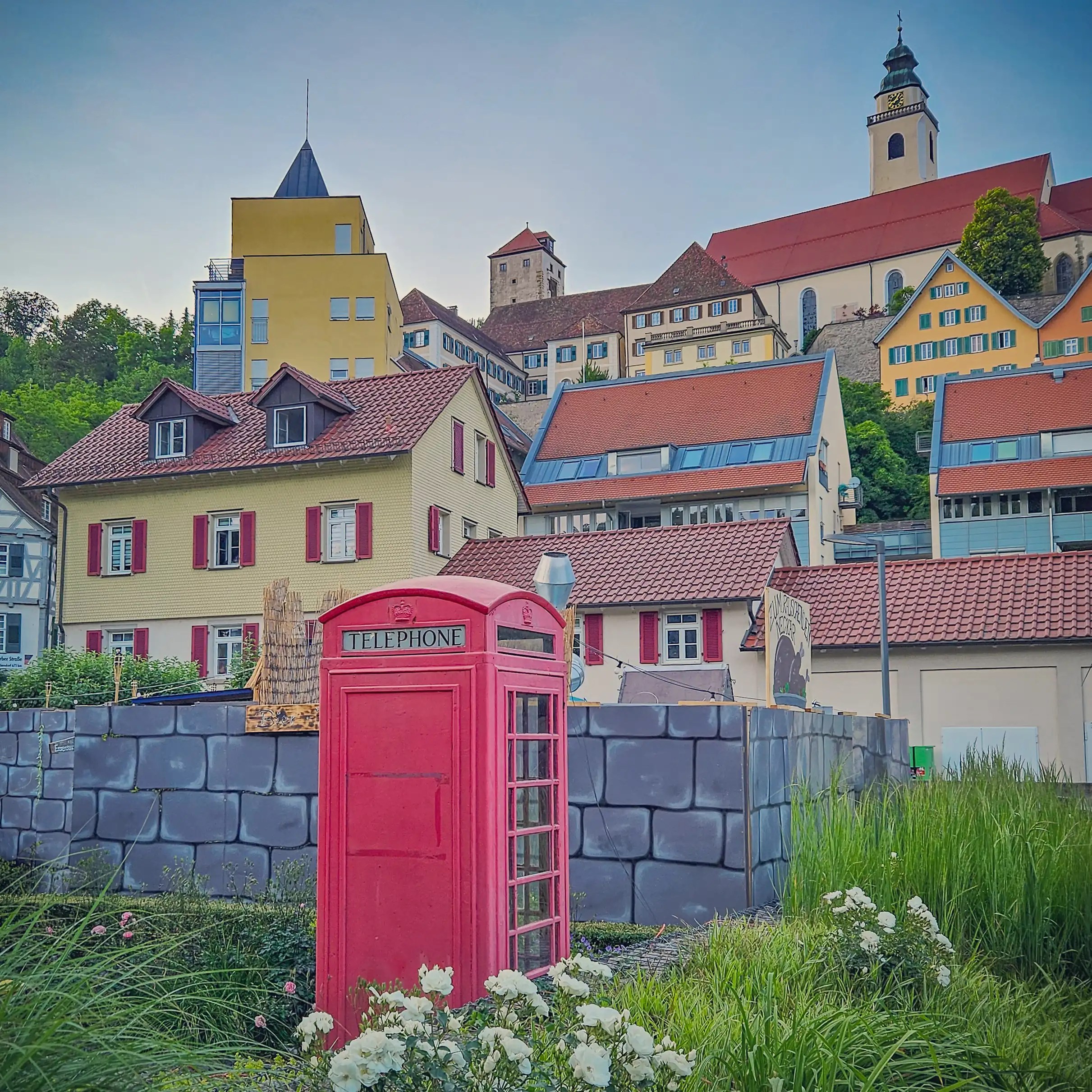 A red British-style telephone booth stands in front of colorful homes and historic buildings in Horb am Neckar.