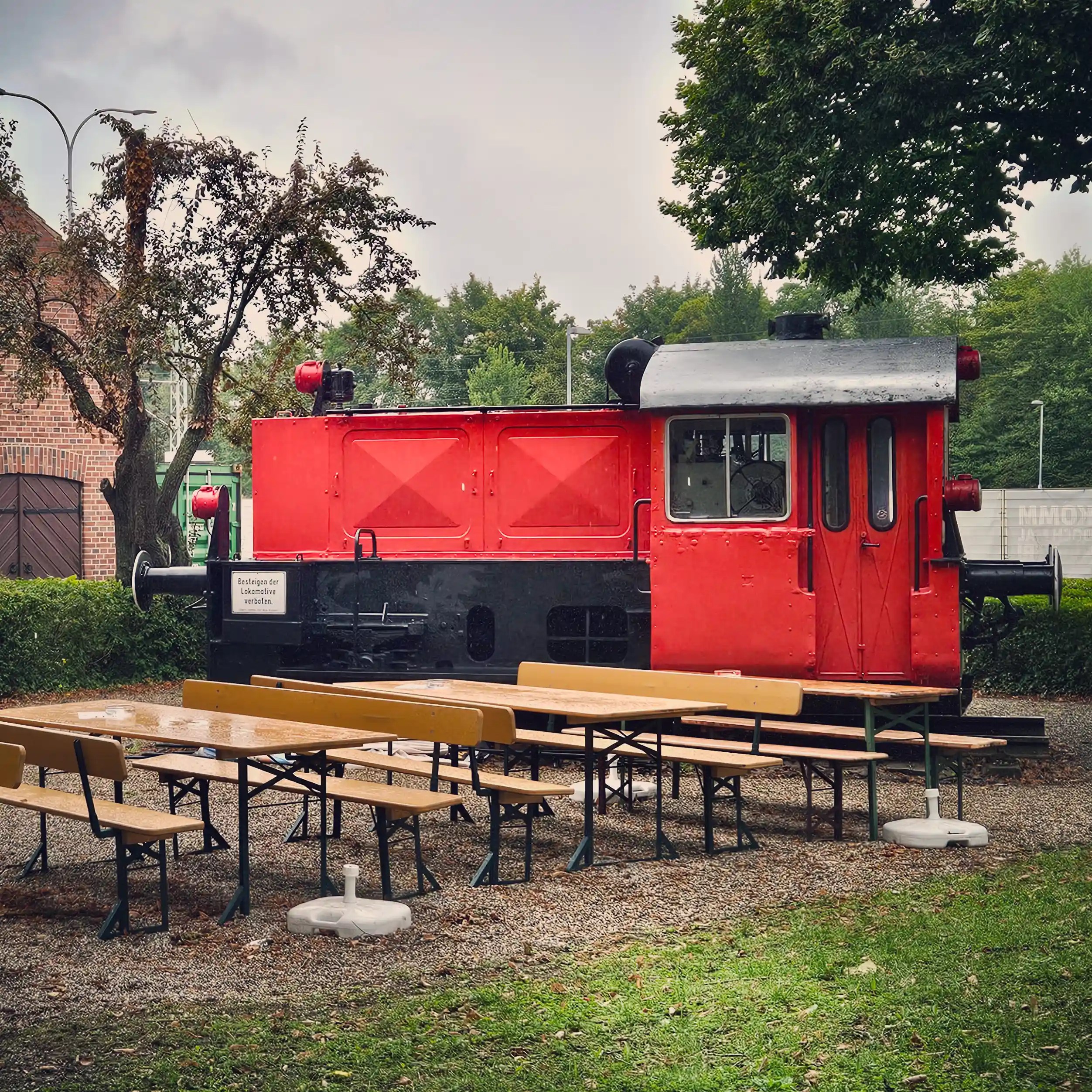 A small red locomotive displayed outdoors beside picnic tables at a beer garden.