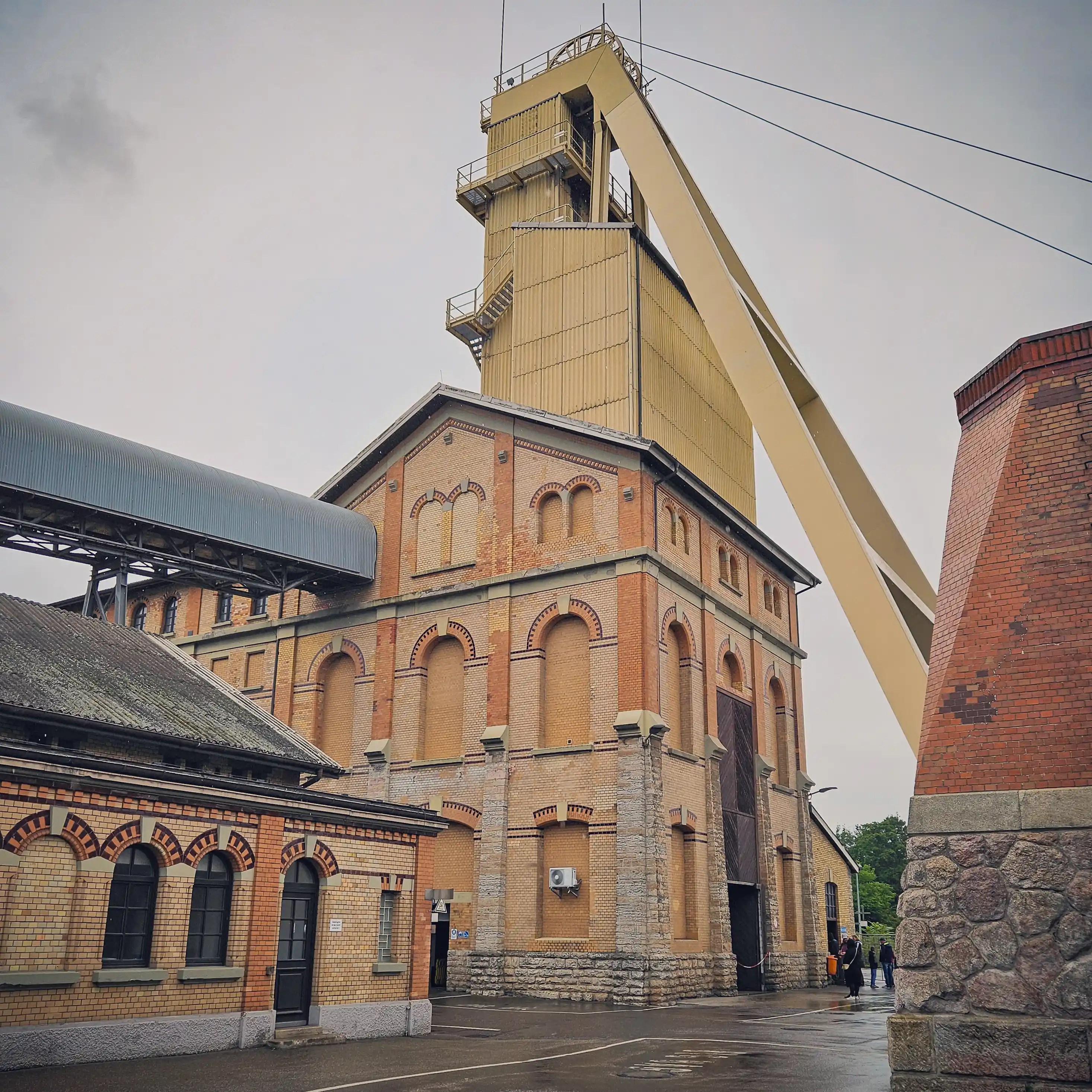 Multiple brick mine buildings with the tall headframe rising in the background at Salzbergwerk Bad Friedrichshall.
