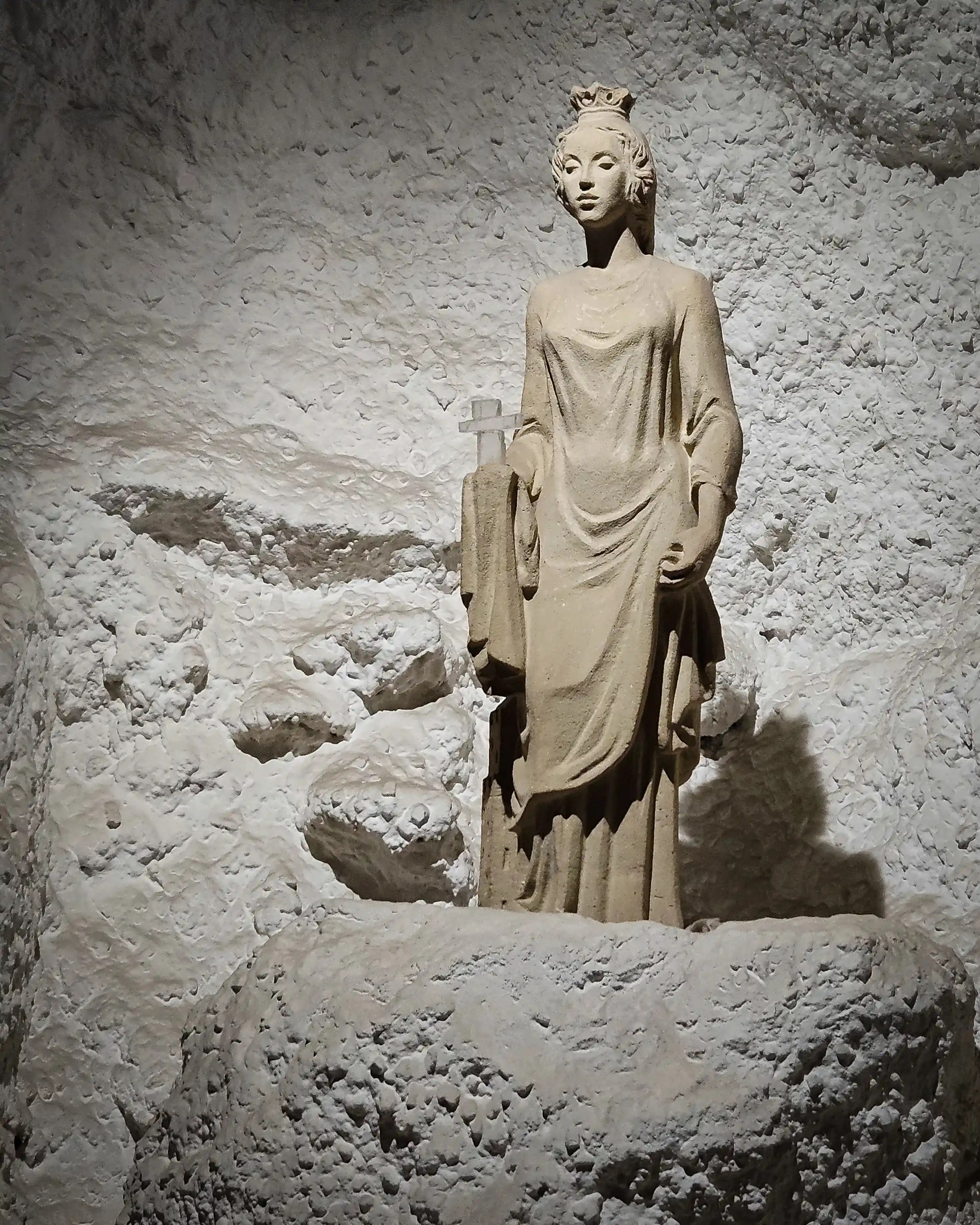 Statue of a crowned woman in a flowing gown with a cross of salt set into a niche in the salt mine wall.