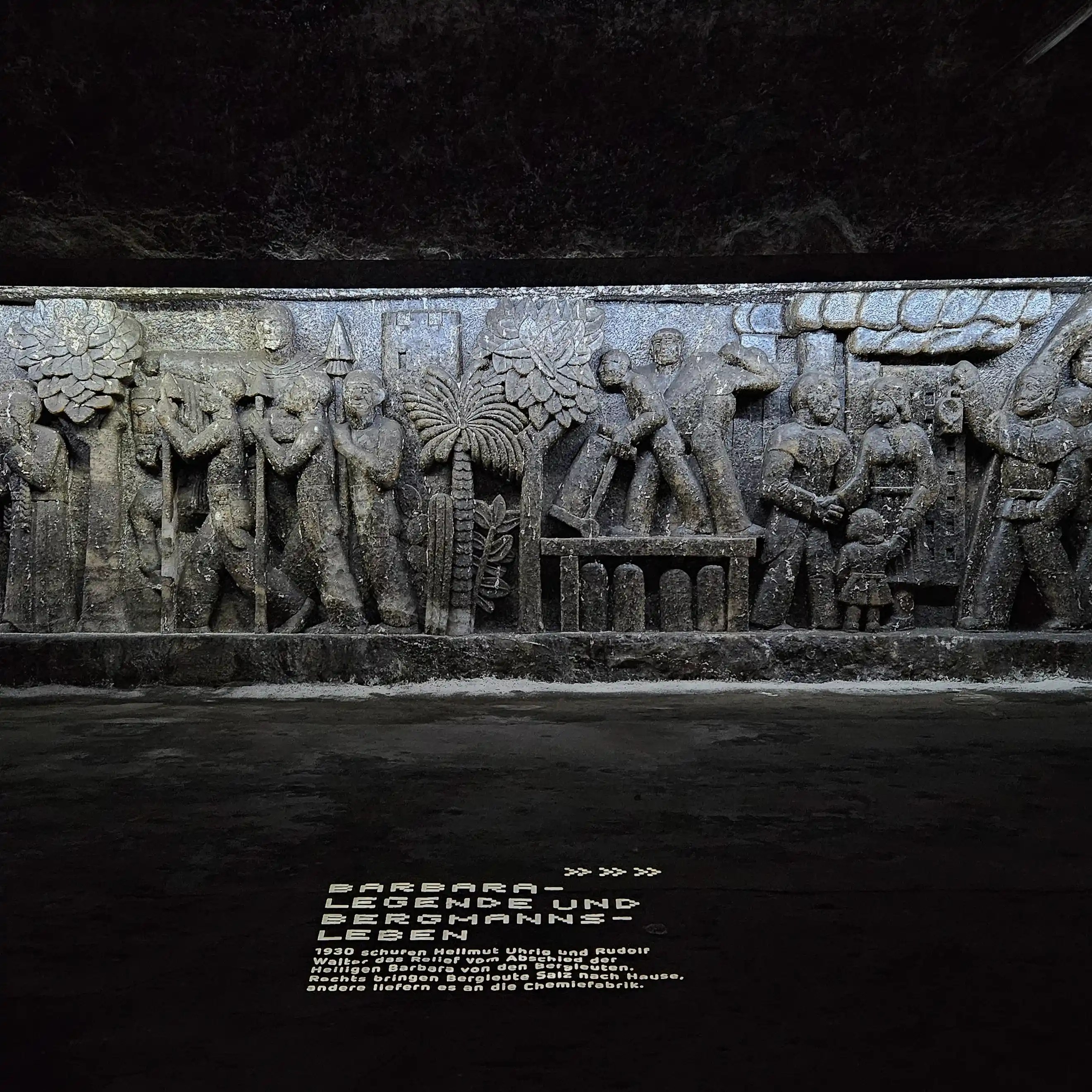 Intricately carved salt wall relief in Salzbergwerk Bad Friedrichshall depicting miners, tools, and scenes from Saint Barbara's legend.