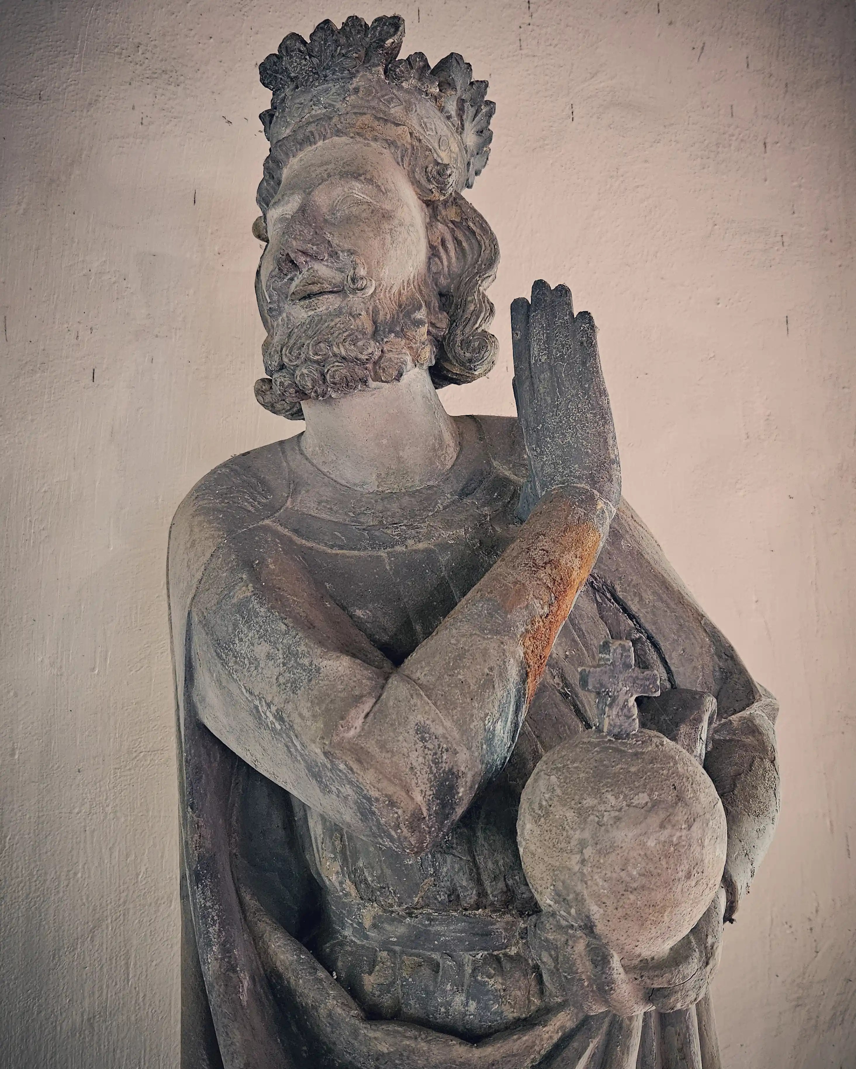 Weathered stone statue of a crowned ruler holding a globus cruciger in Bad Wimpfen.