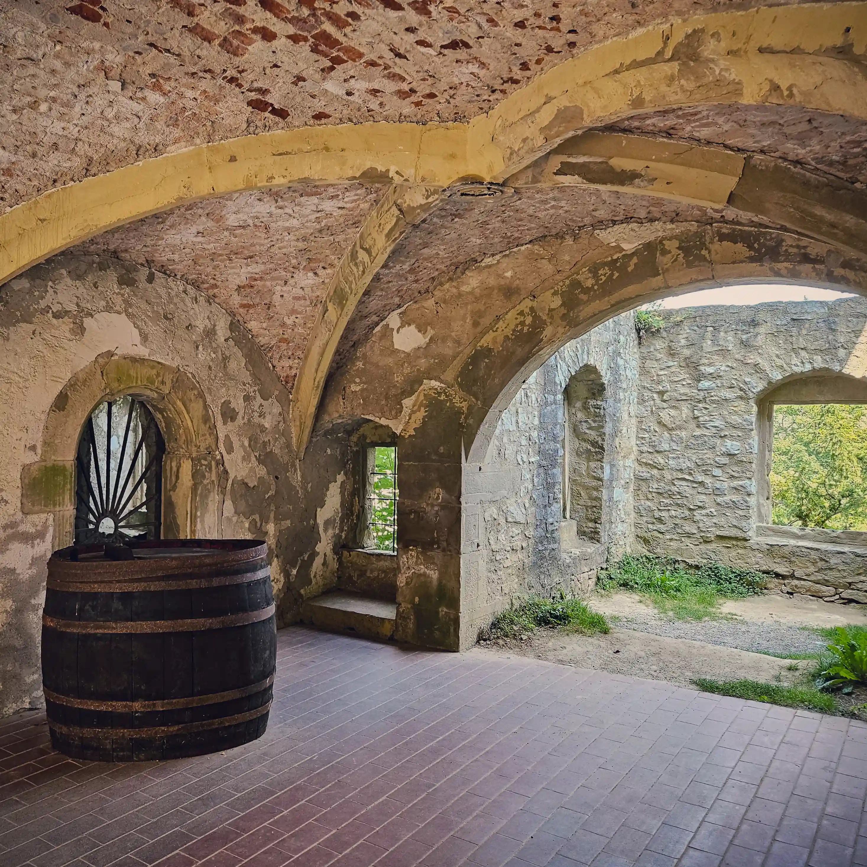 Vaulted stone room with an old wine barrel opening to ruined castle walls at Burg Hornberg.