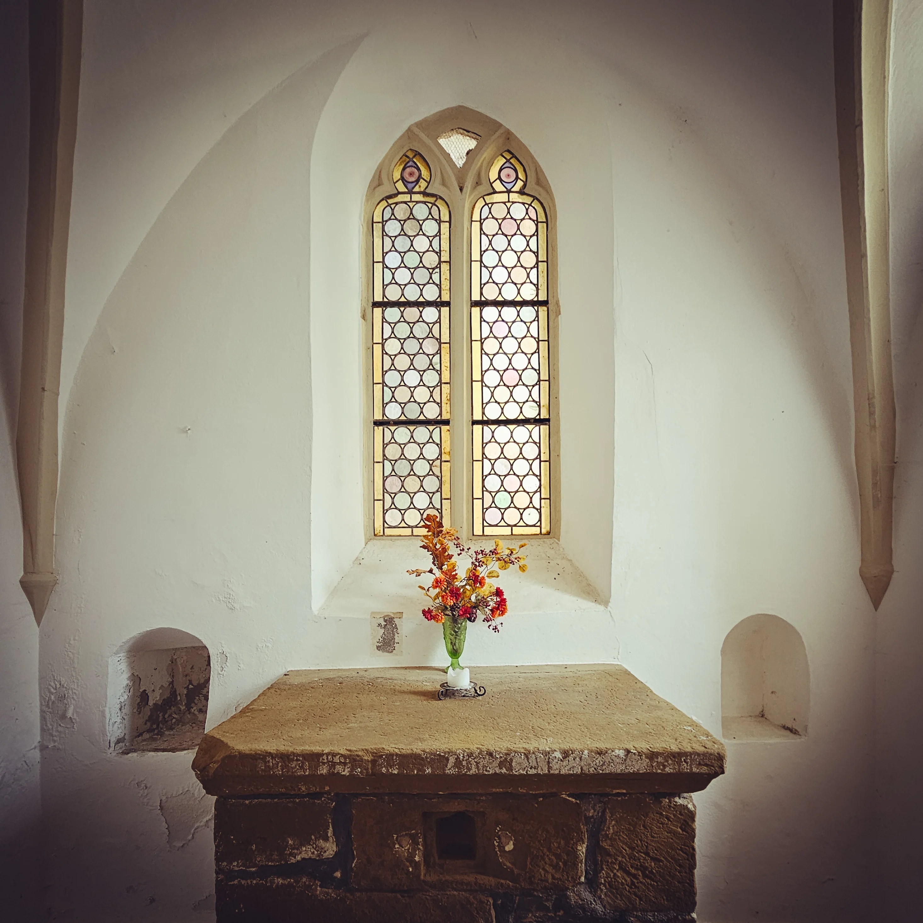 Small Gothic window with patterned glass and a vase of flowers on a stone altar at Burg Hornberg.