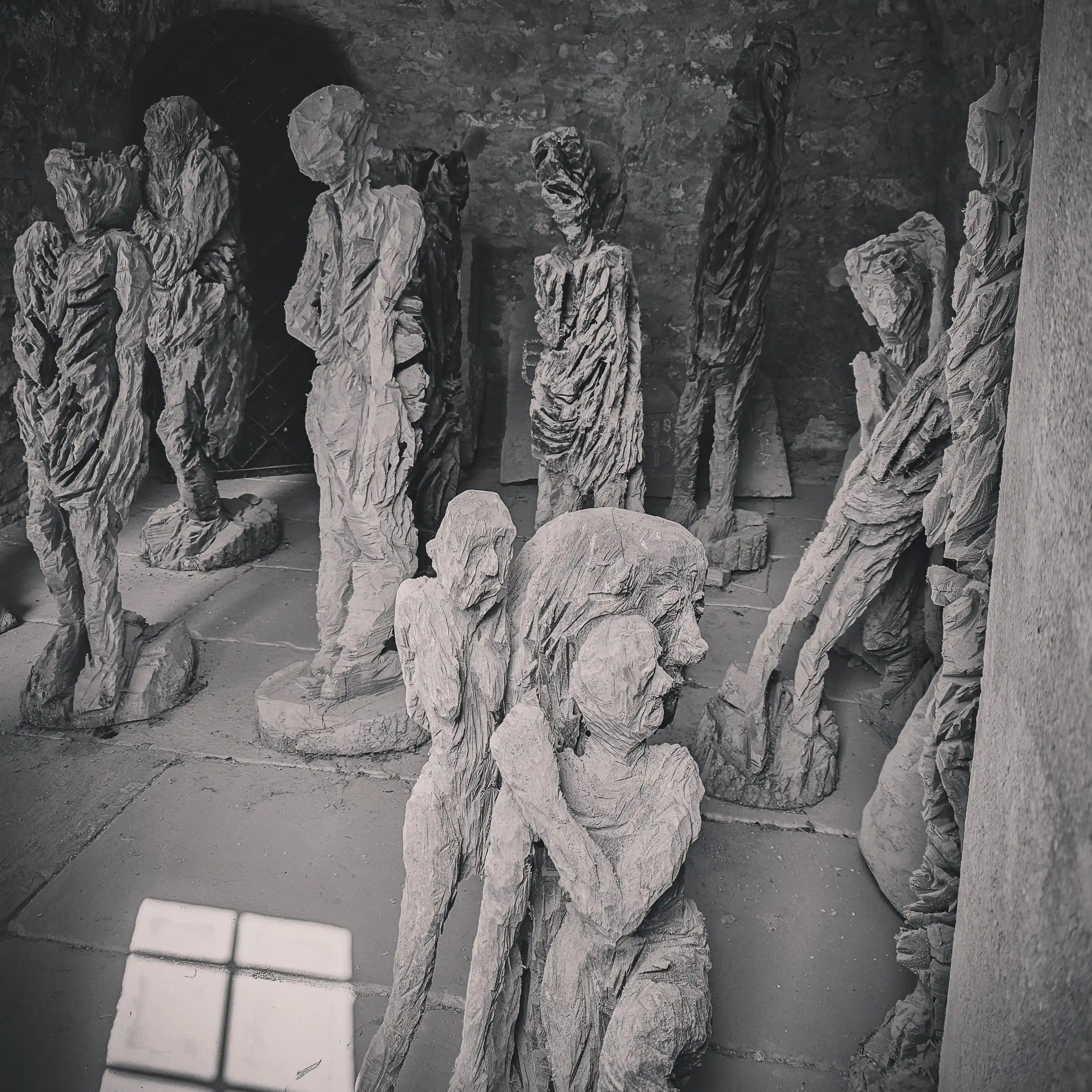 Group of rough-hewn figurative sculptures in a dim stone chamber, Burg Hornberg.